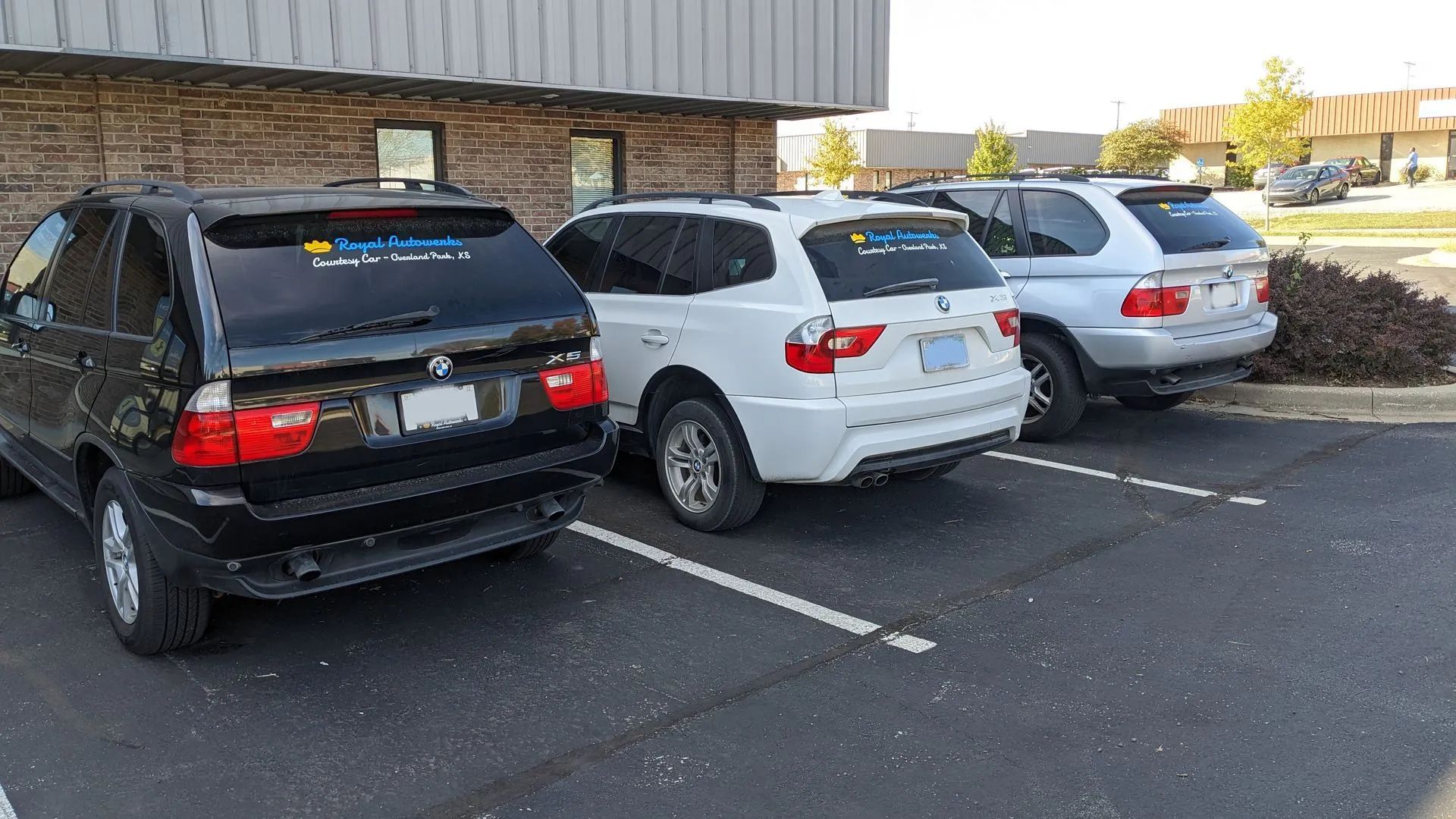 Three BMW SUVs parked in a parking lot: black, white, and silver.