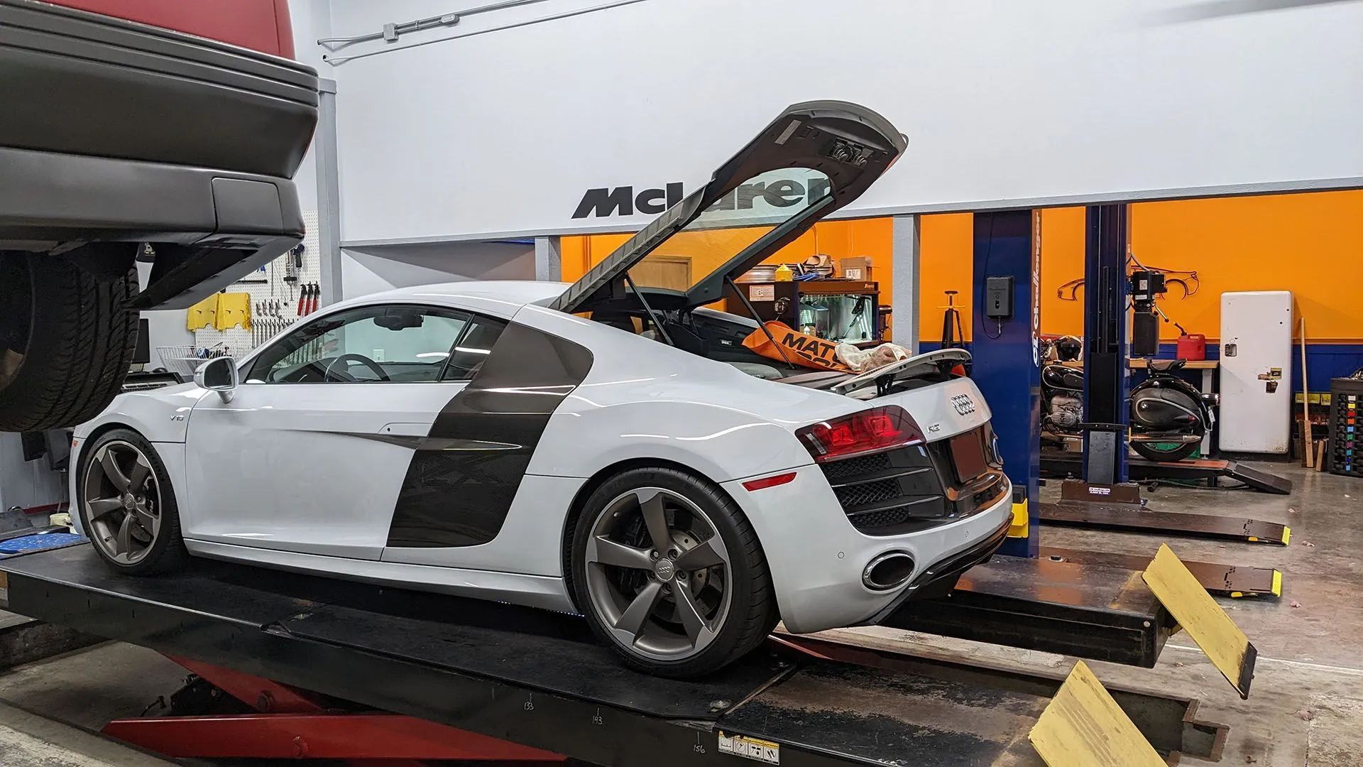 White Audi R8 coupe with open engine bay on a lift in a garage.