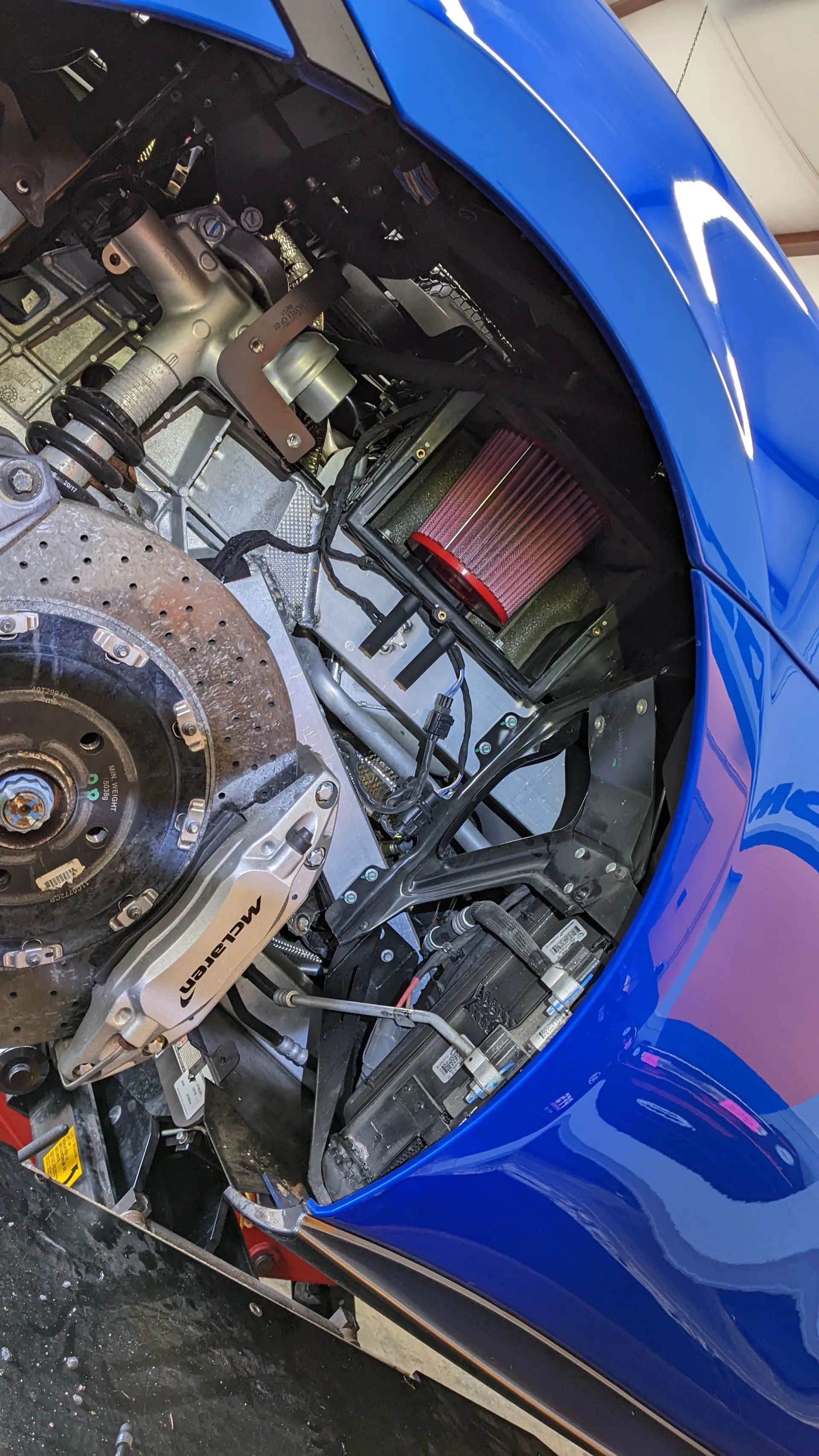 Blue car's engine bay, showcasing the engine components, brake disc, and air filter.