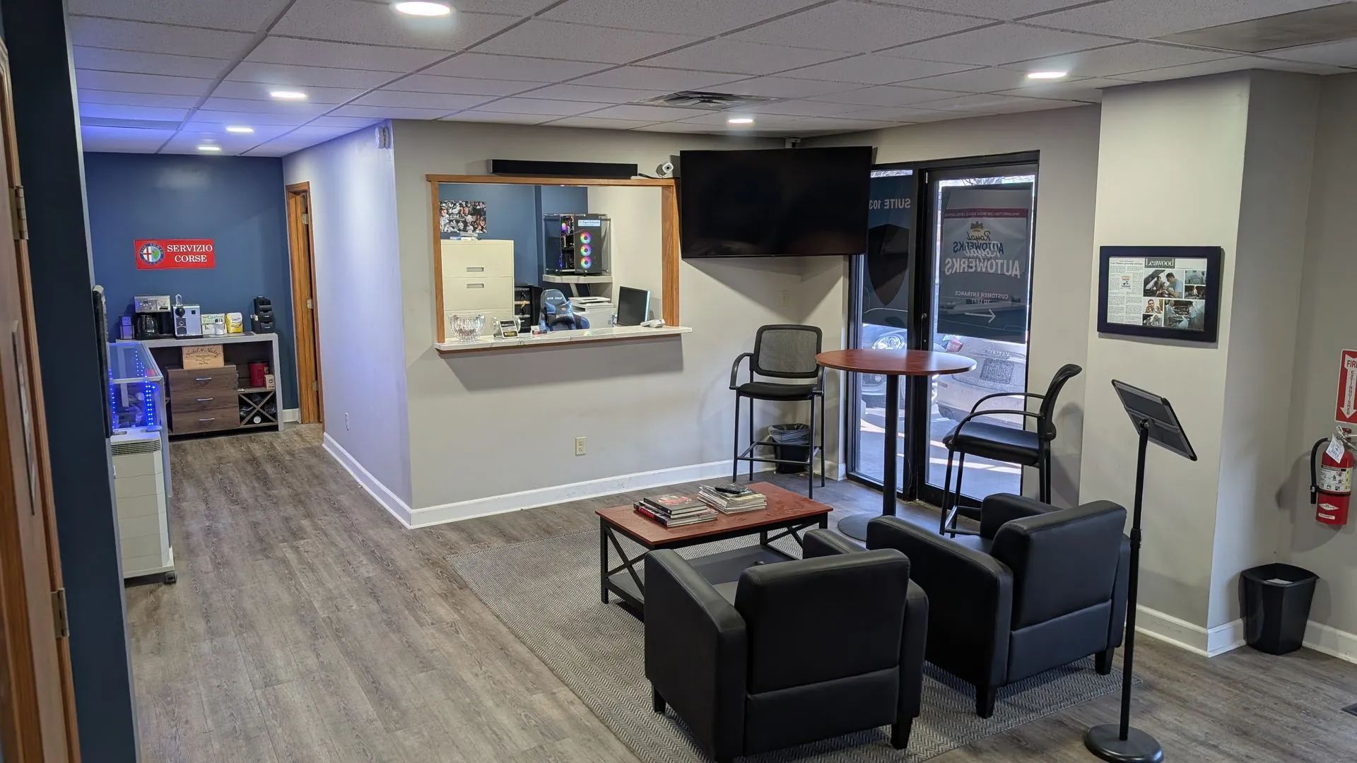 Waiting room with gray flooring, two black chairs, a coffee station, and a TV.