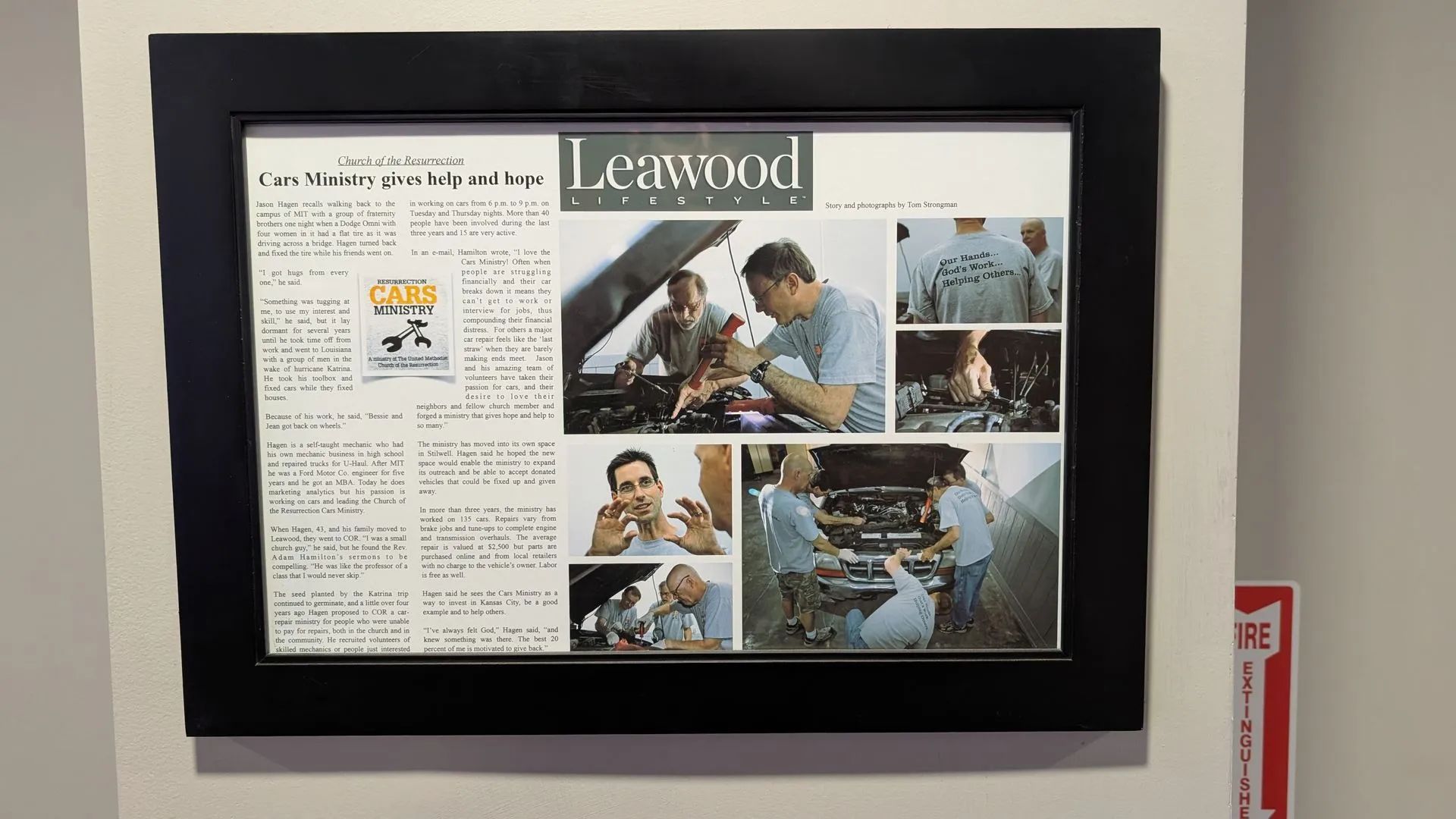 Framed newspaper page with photos of mechanics working on a car and text about the topic, mounted on a wall.