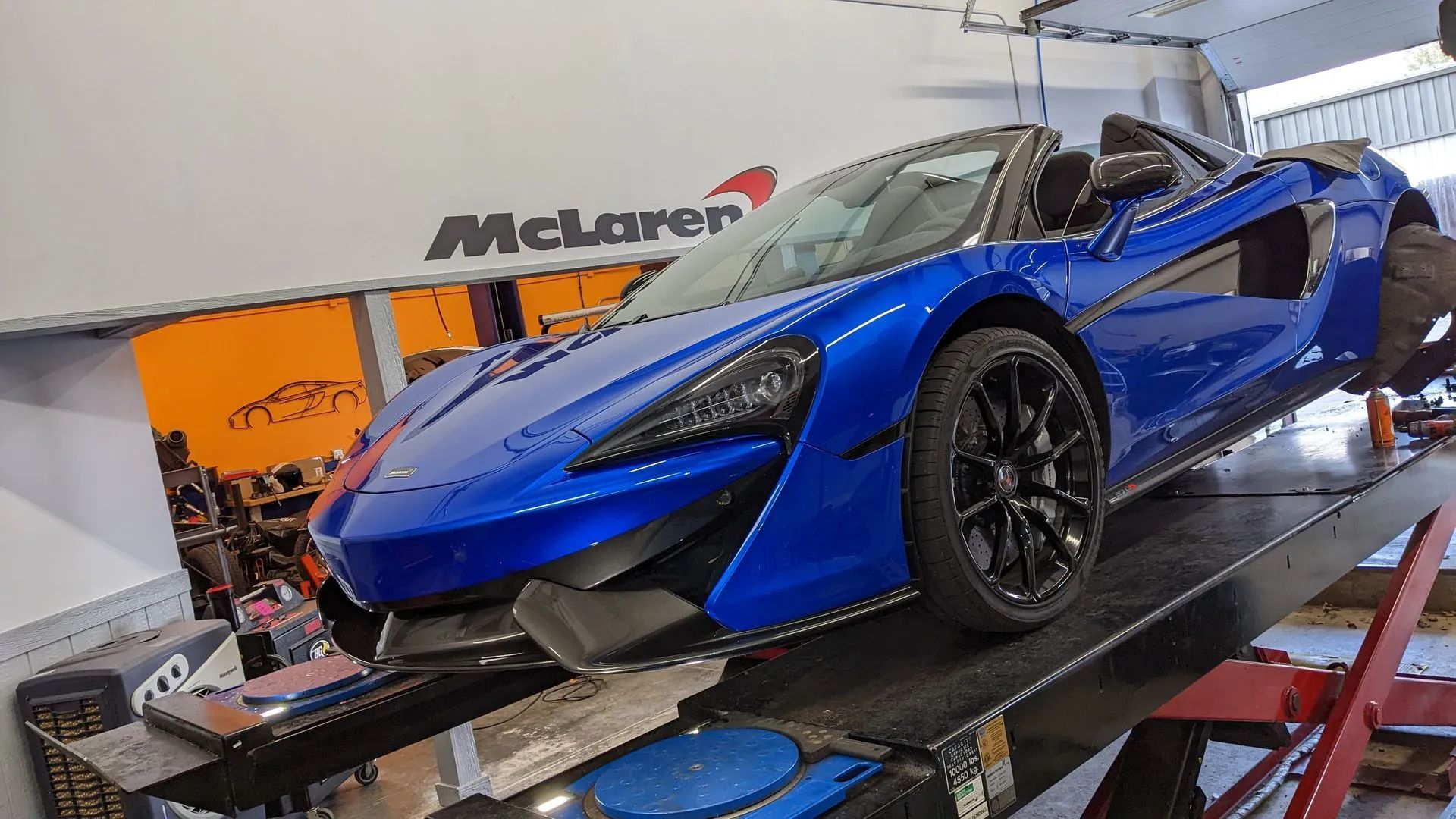 Blue McLaren convertible on a lift in a McLaren service center.