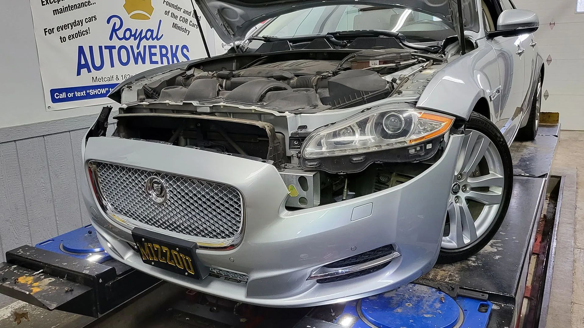 Silver Jaguar sedan with open hood in a repair shop.