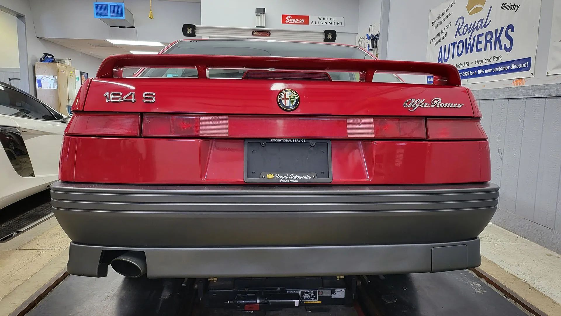Red Alfa Romeo 164 Q4 sports car rear view. Black bumper, license plate, and spoiler. Inside a garage.