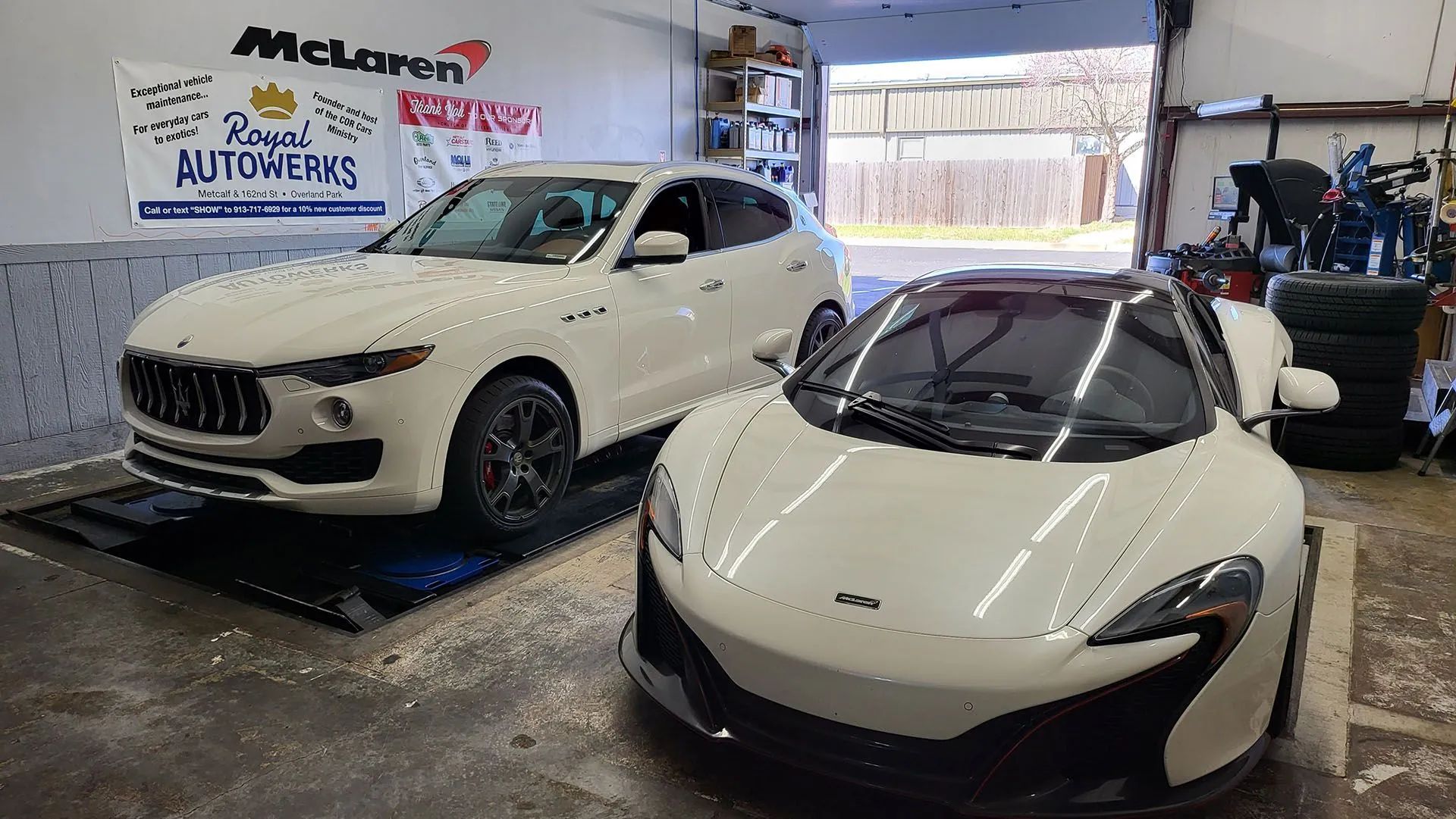 White Maserati SUV and white McLaren sports car inside a garage with open bay door.