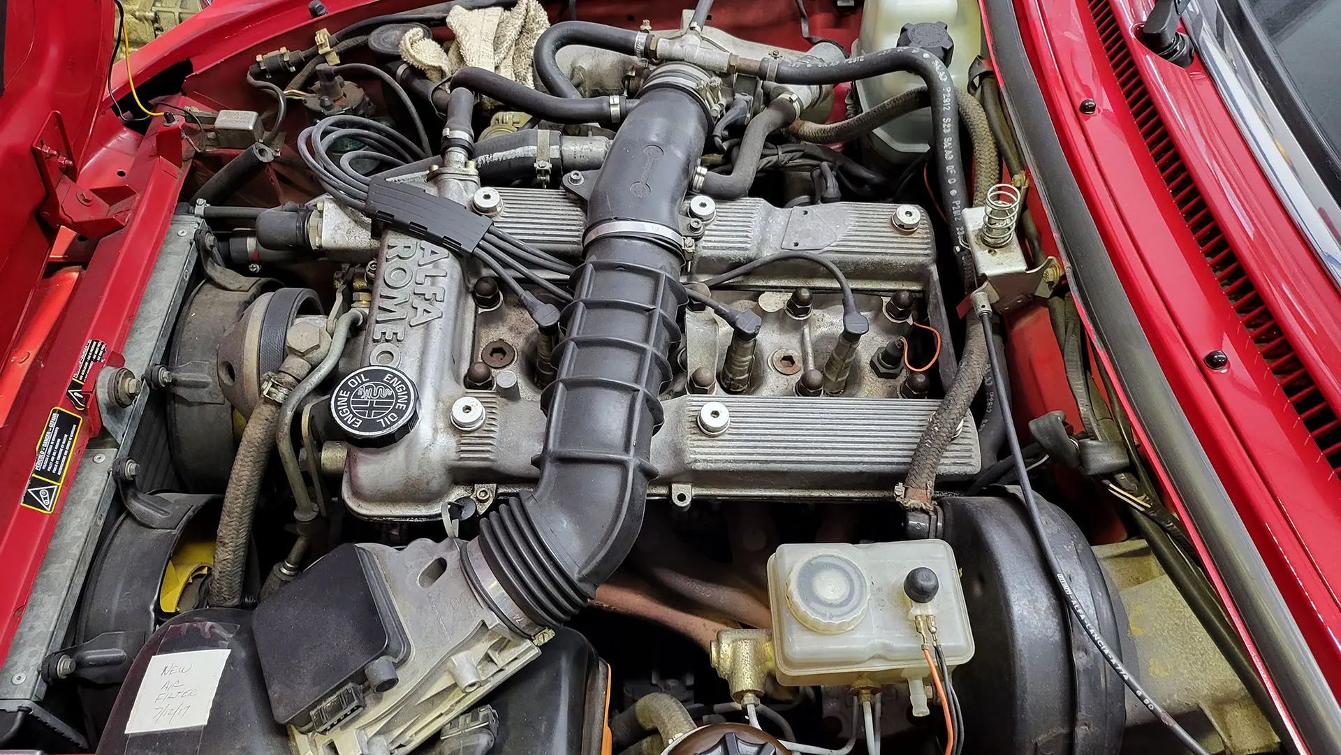 Red car engine bay with black air intake tube and various engine components.