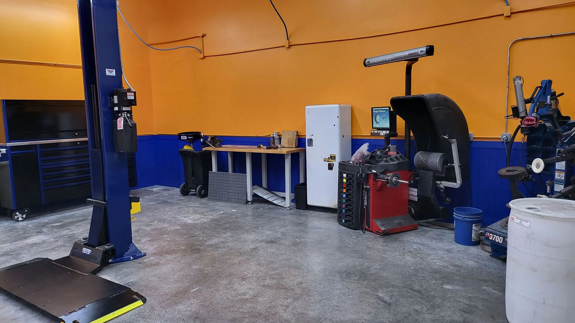 A car repair shop interior with blue lift, orange walls, and repair equipment.