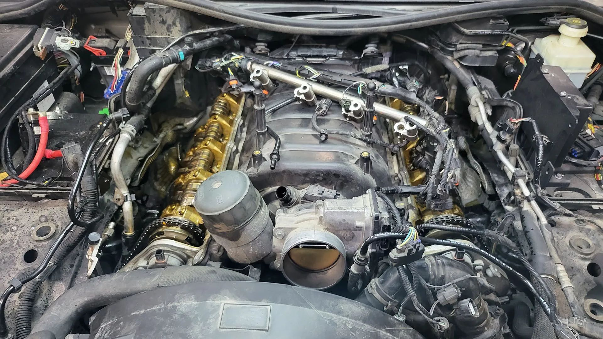 Car engine bay with parts removed, revealing engine components and wiring.