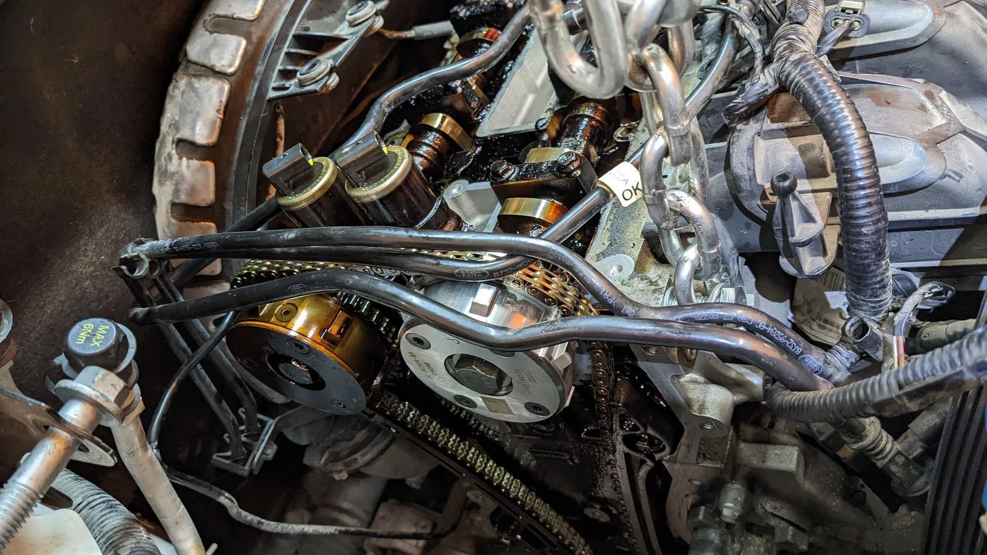 Open car engine with exposed parts, oil-stained, showing camshafts and chains, undergoing repair.