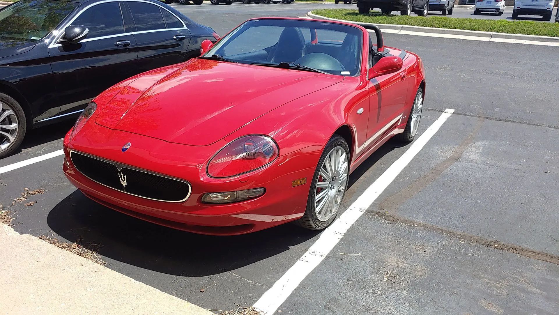 Red Maserati Spyder convertible parked in a parking space on a sunny day.