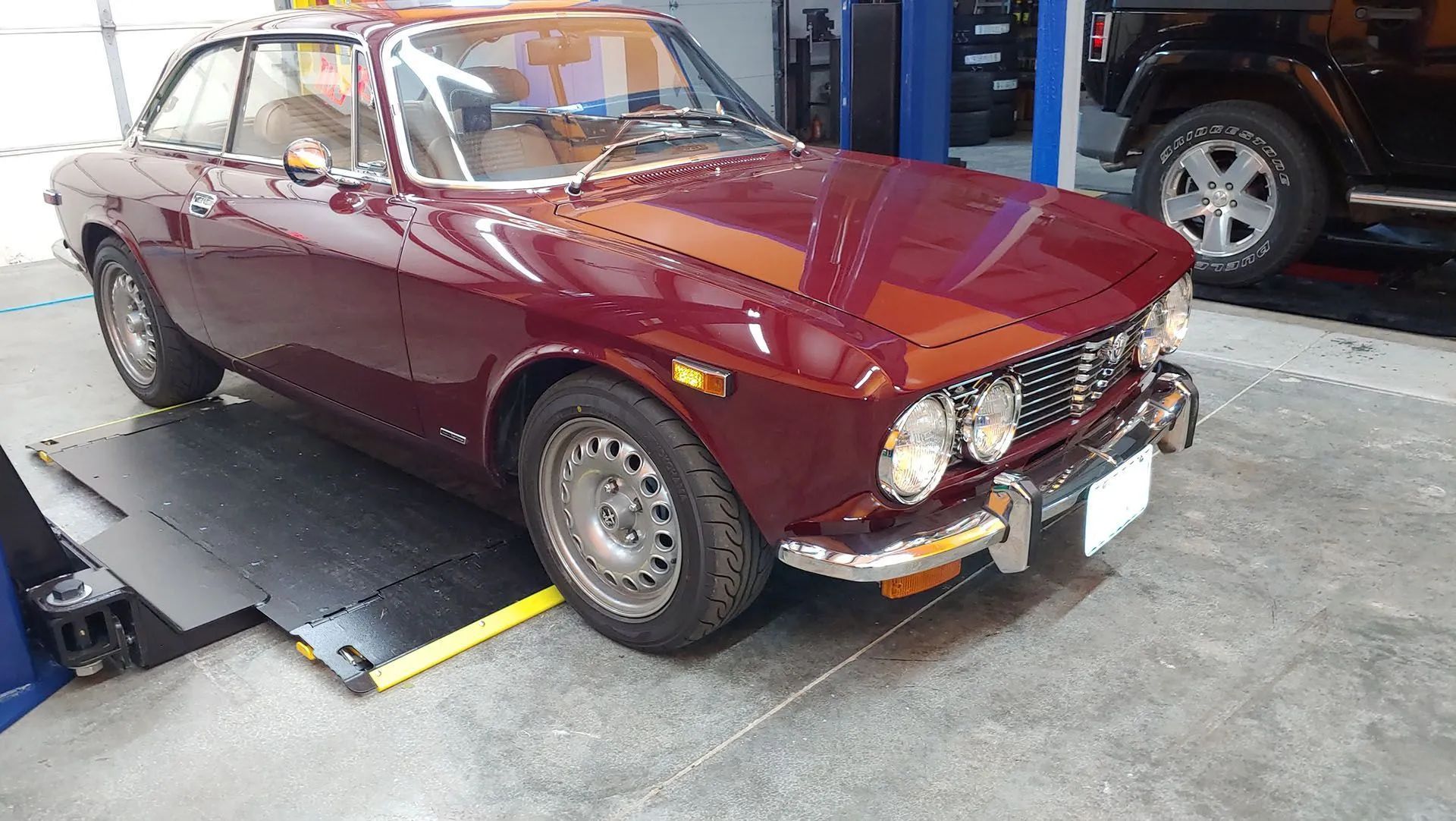 Burgundy vintage sports car on a lift in a garage.