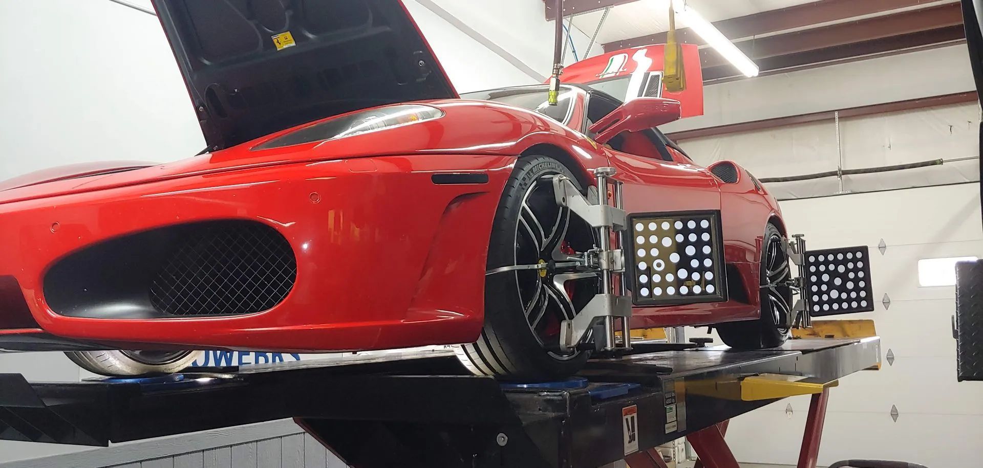 Red sports car on a lift in a garage, undergoing wheel alignment, with gauges attached.