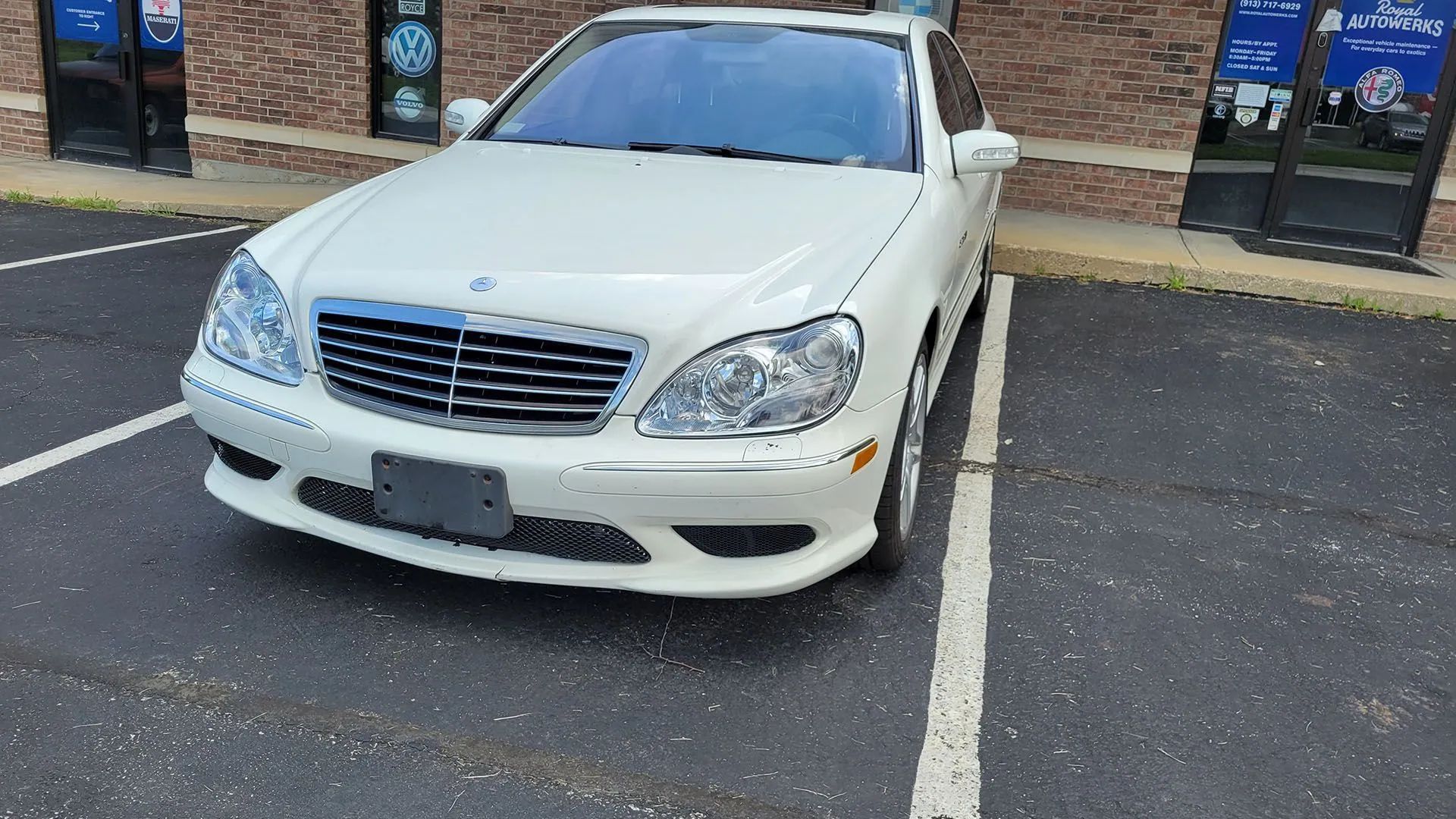 White Mercedes-Benz sedan parked in a parking space in front of a store.