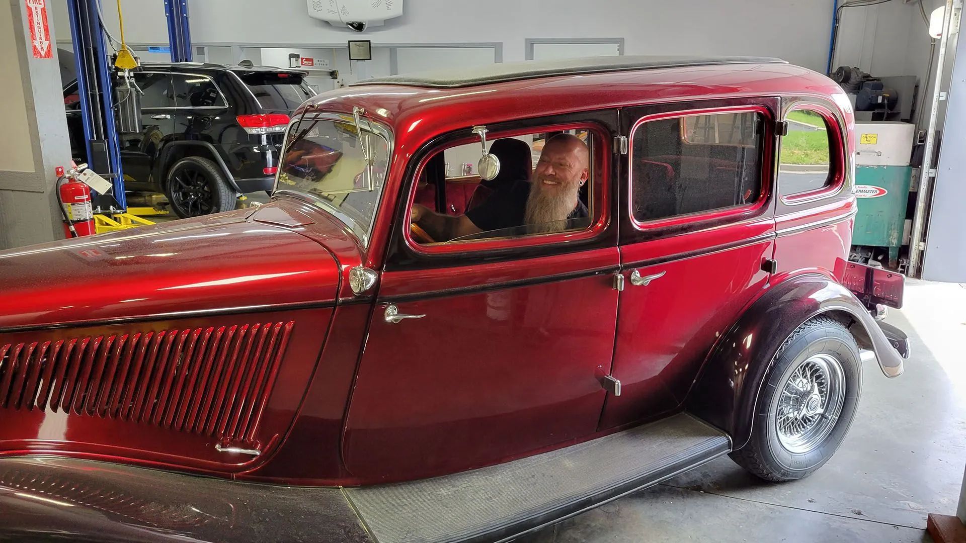 Red vintage car inside a garage; person in driver's seat.