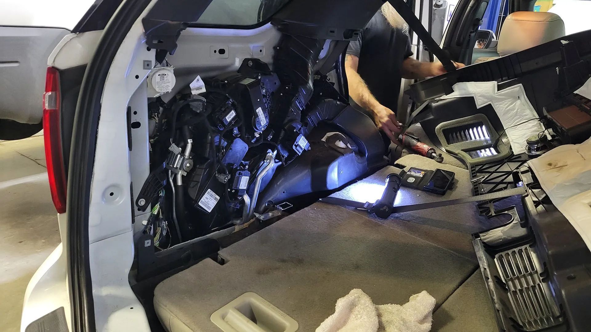 Person working on the interior of a white car's rear, exposing wires and components.