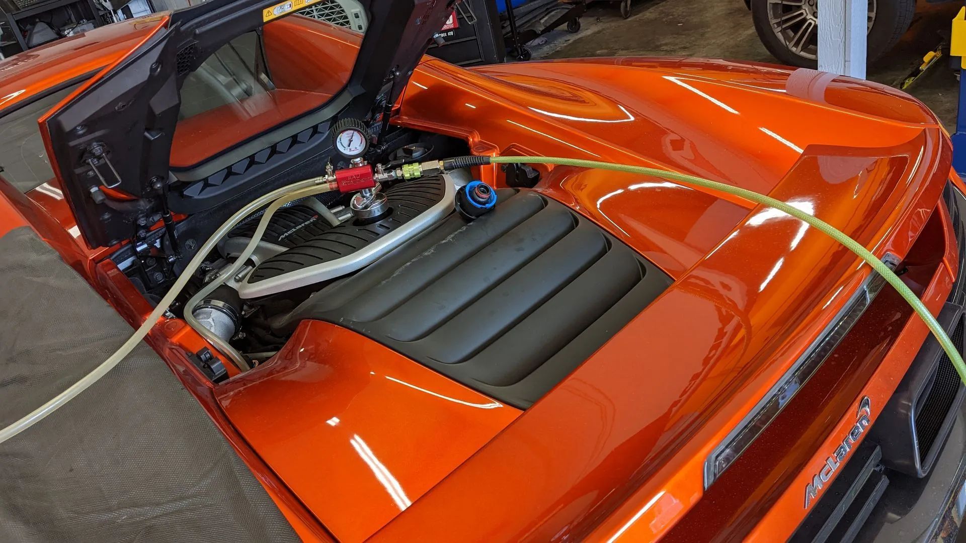 Orange car engine bay with opened hood, hoses, and instruments.