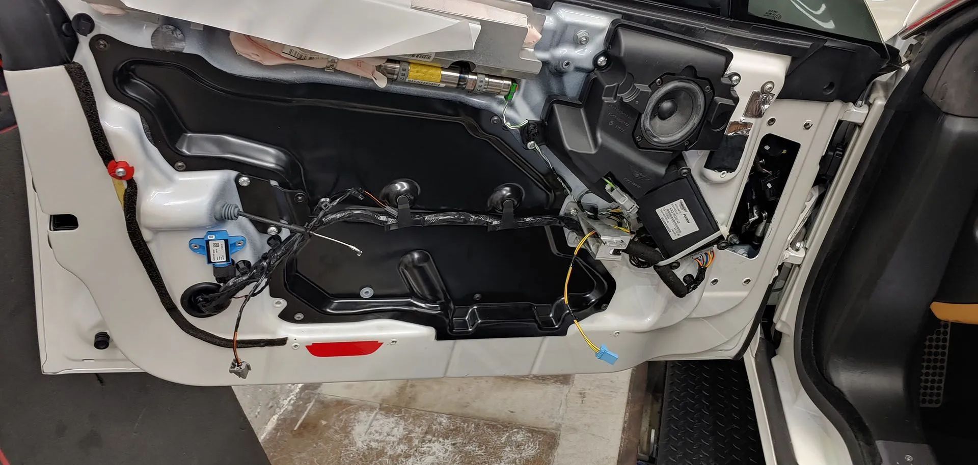 Car door interior with components exposed. Wires, speaker, and various parts are visible.