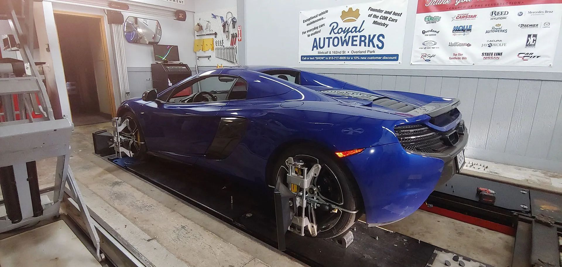 Blue sports car on a lift in a garage, next to a sign for Royal Autowerks.