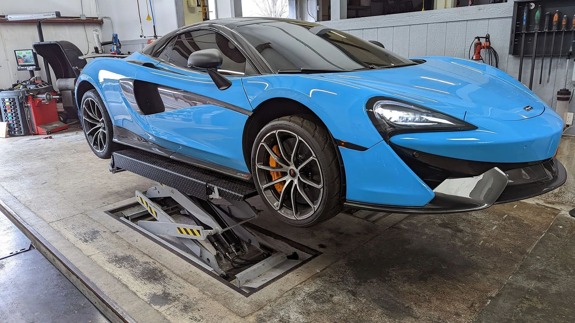 Blue McLaren sports car on a hydraulic lift in a repair shop.