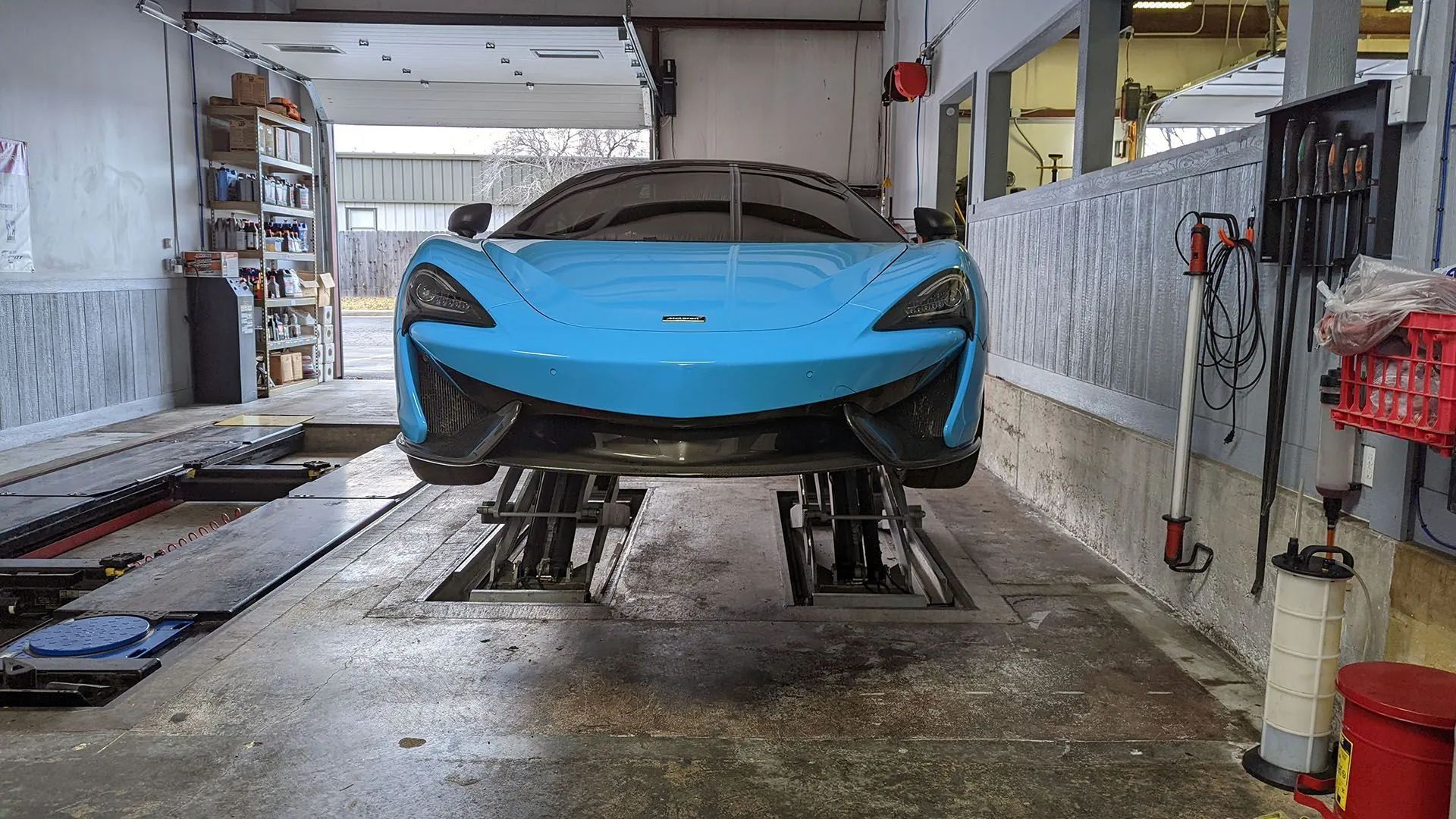 Blue McLaren sports car on a hydraulic lift in a repair shop.