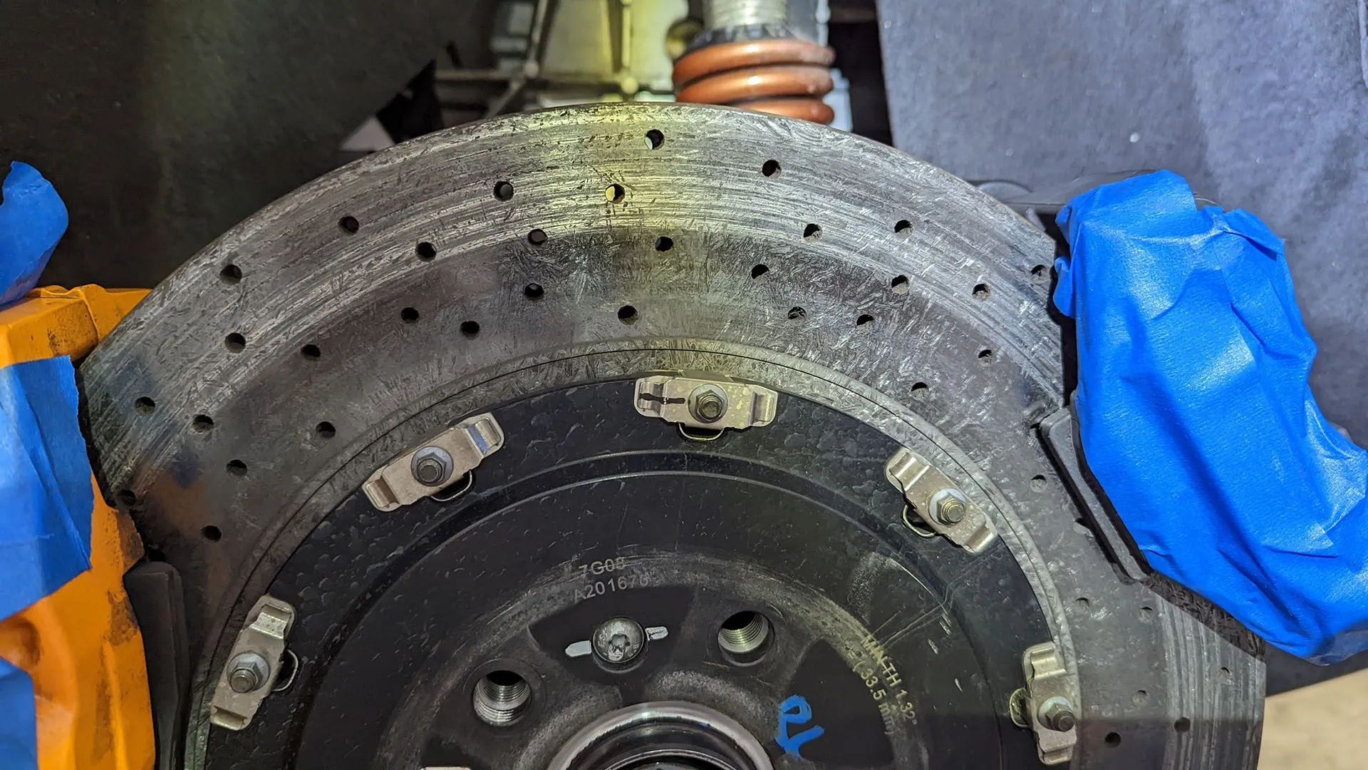 Close-up of a car's brake rotor with drilled holes, covered in dust, with a blue caliper.