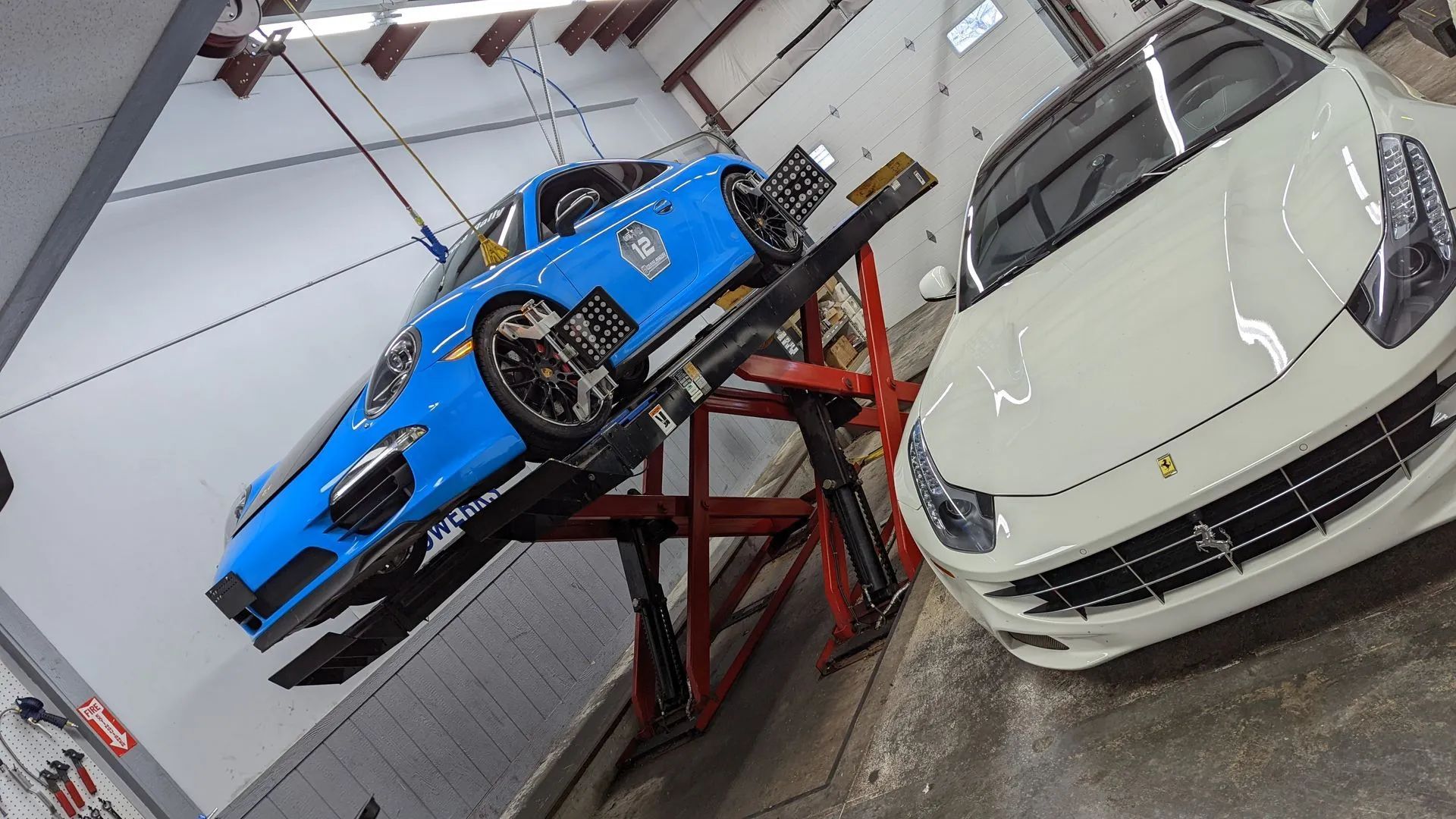Blue car on a lift in a garage next to a white Ferrari.