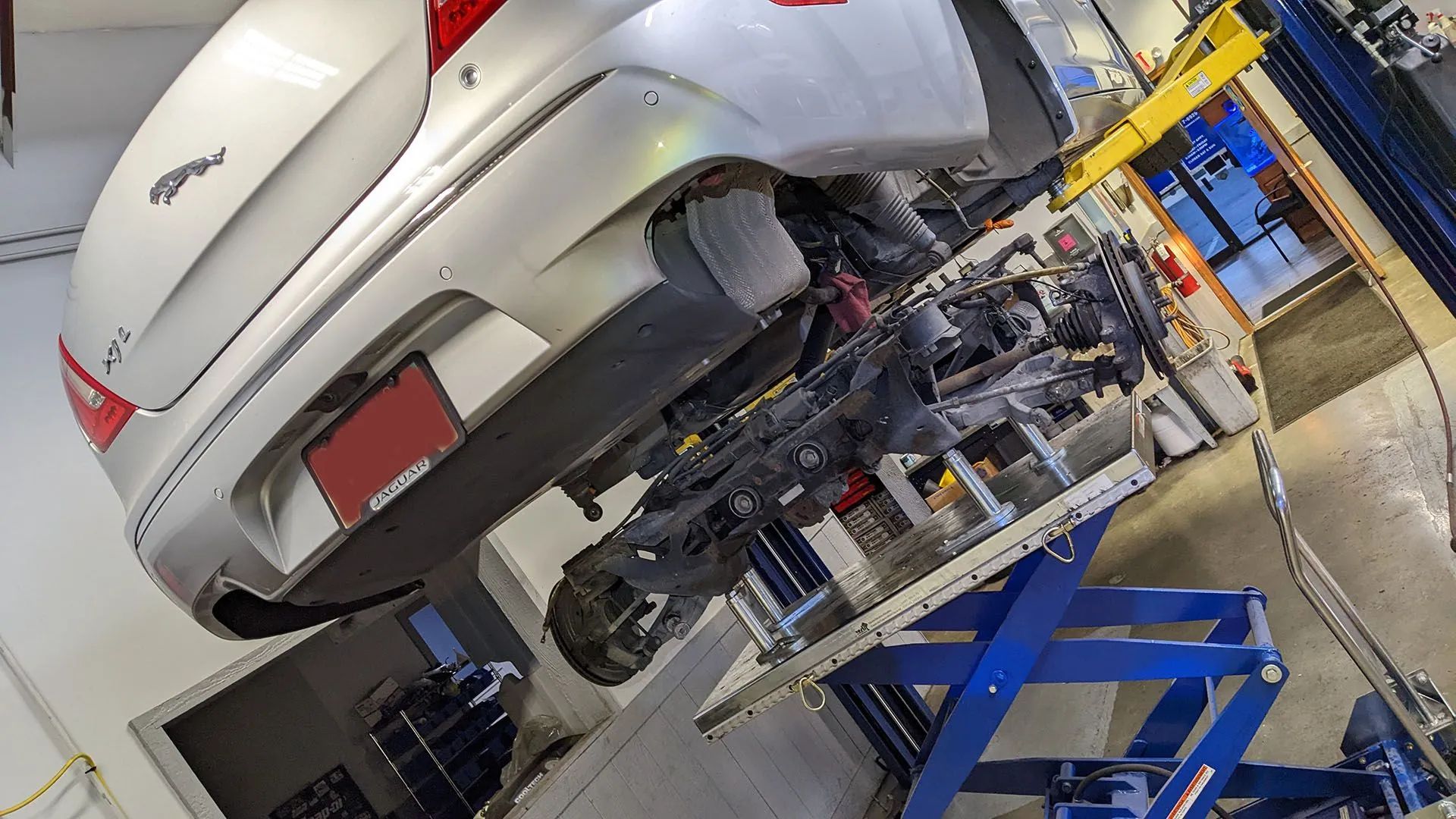 Silver Jaguar car raised on a lift for repair in a mechanic's shop.