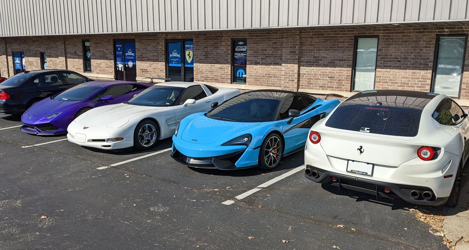 Row of luxury sports cars parked in front of a building: black, purple, white, blue, and white vehicles.