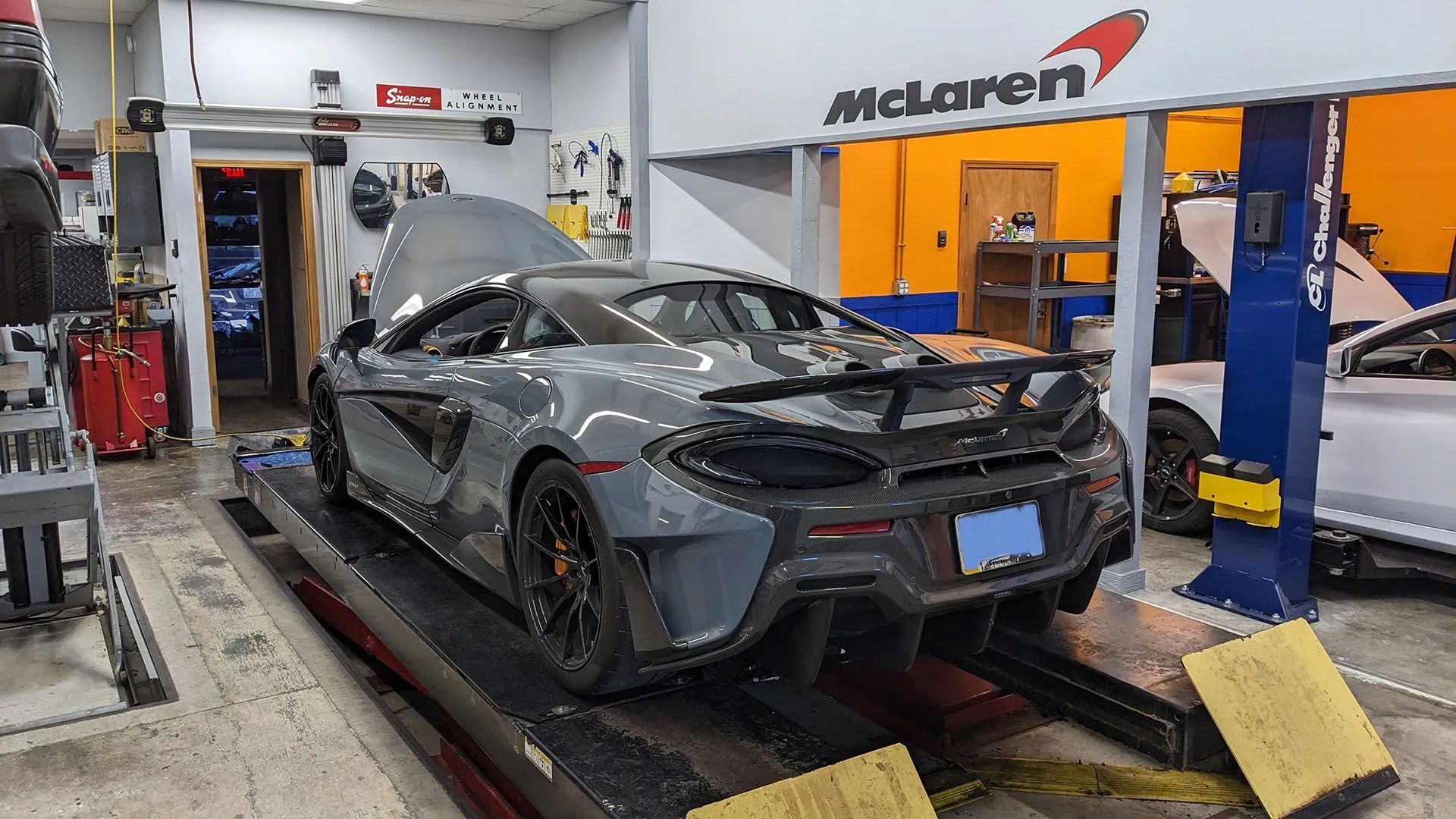 Gray McLaren sports car on a lift in a garage with the hood open, under a 