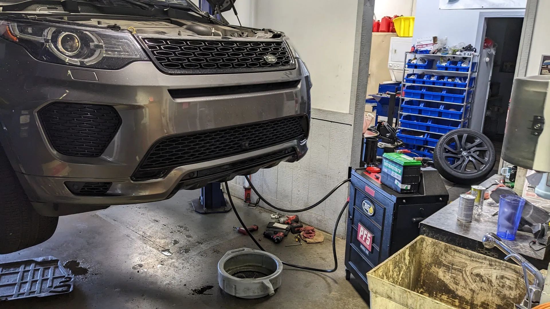 SUV being repaired in a garage. Car is elevated, oil pan and tools are on the floor.