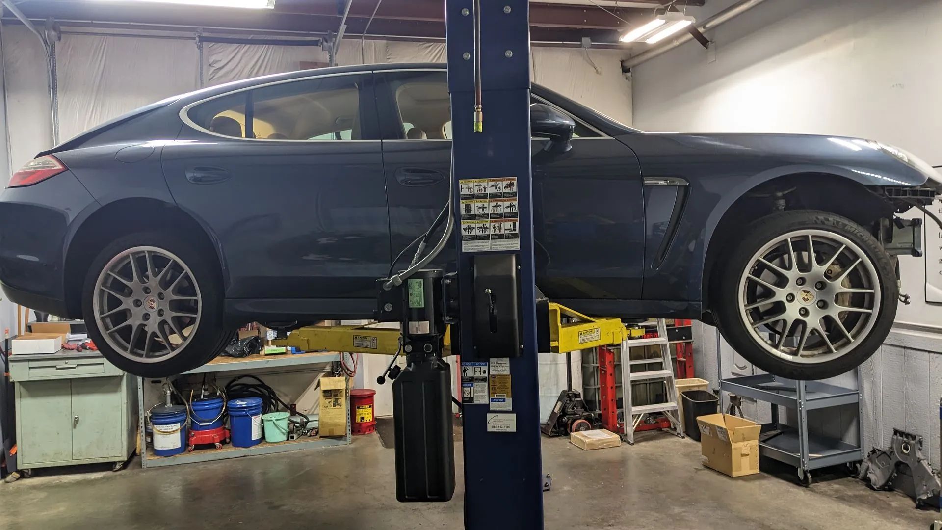 Dark blue car on a lift in a garage, missing its front bumper.