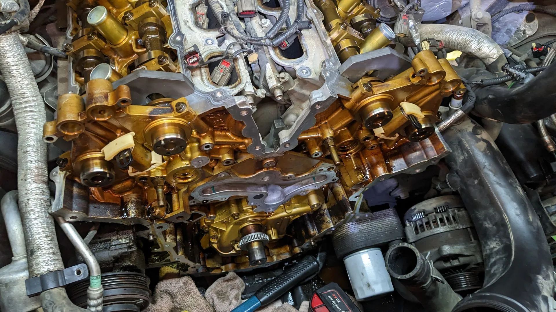 Engine components, coated in gold-colored fluid, exposed in an engine bay.