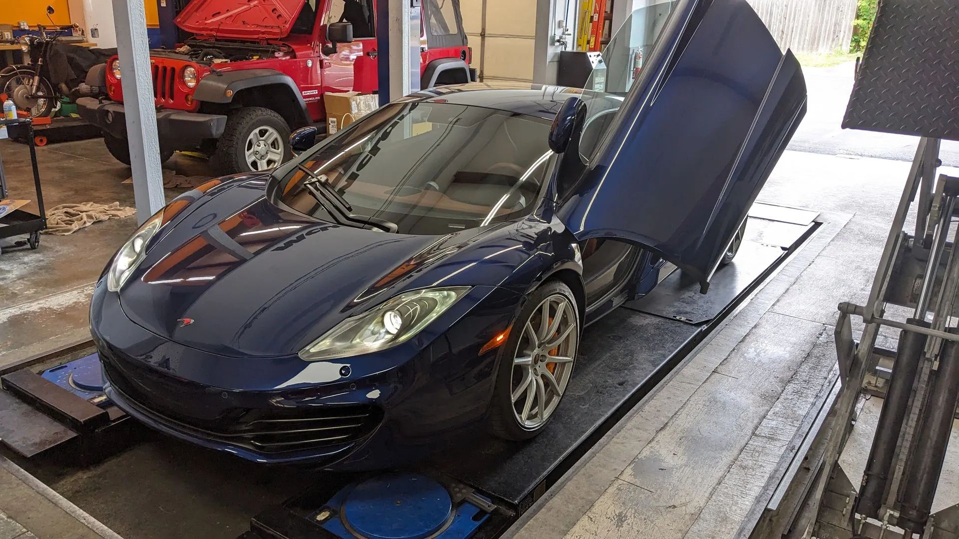Blue McLaren sports car with doors open on a lift in a garage.
