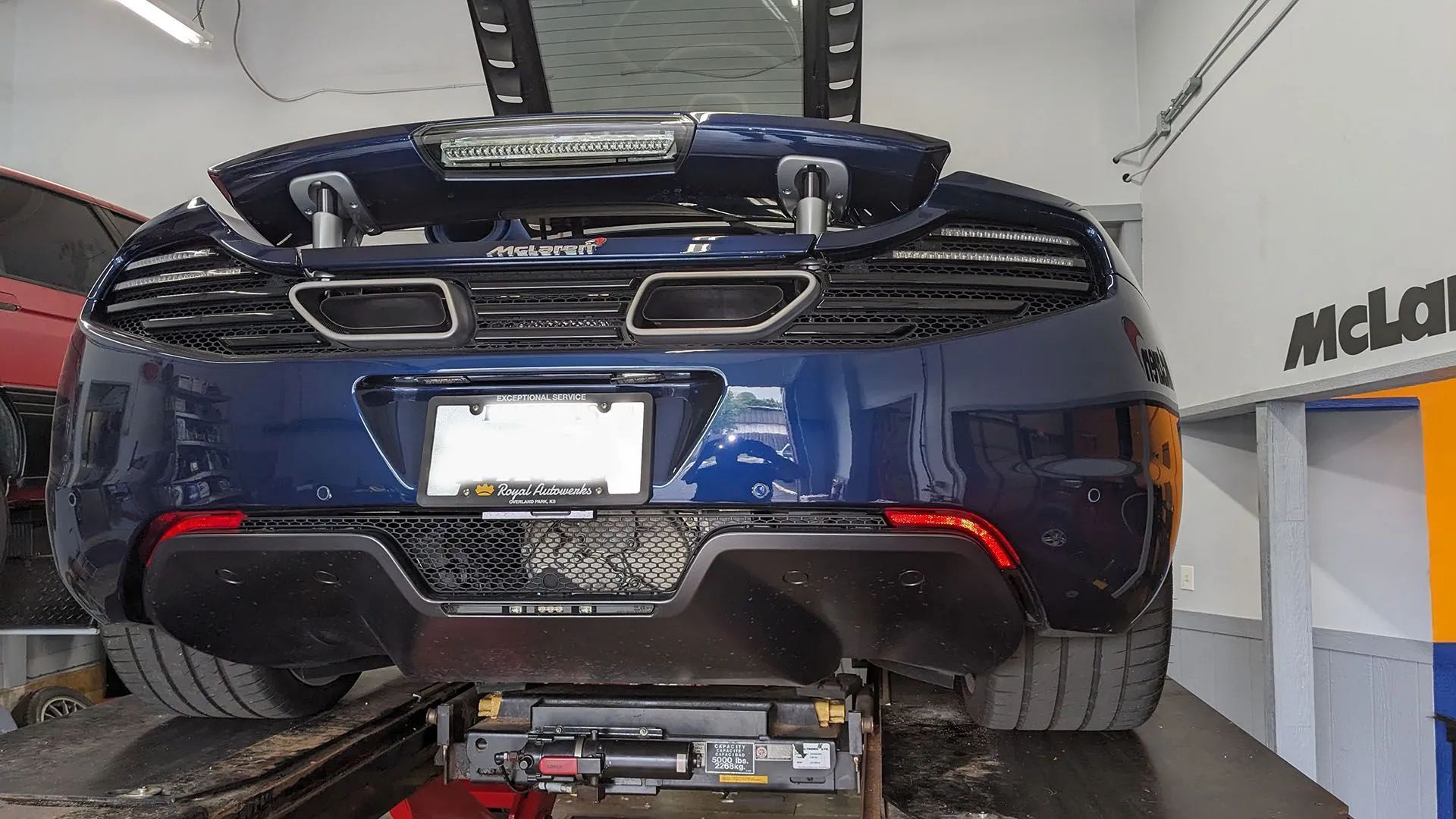 Blue McLaren sports car on a lift, rear view. Exhaust pipes visible, garage setting.