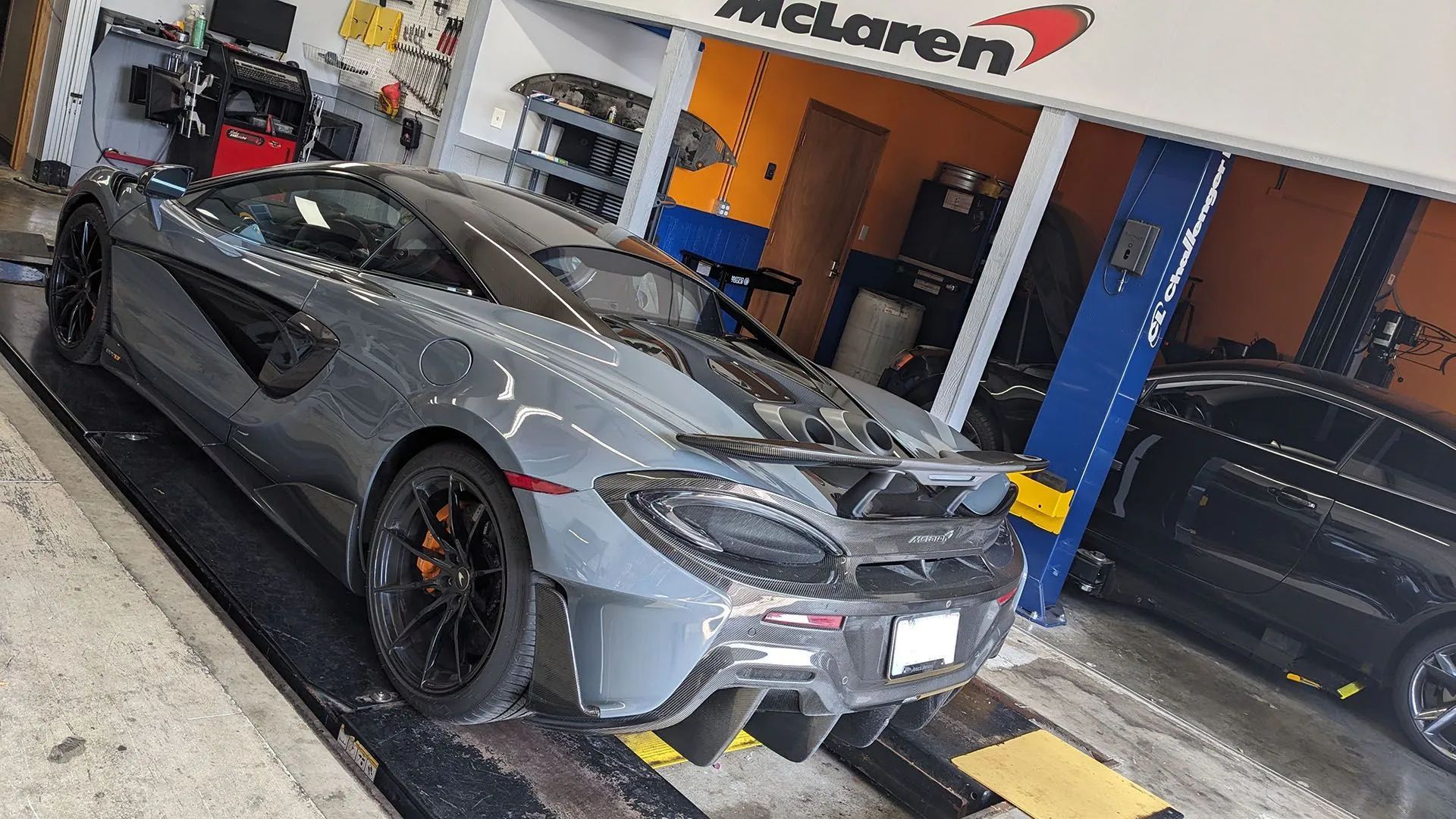 Gray McLaren sports car on a lift in a garage with a McLaren sign above.