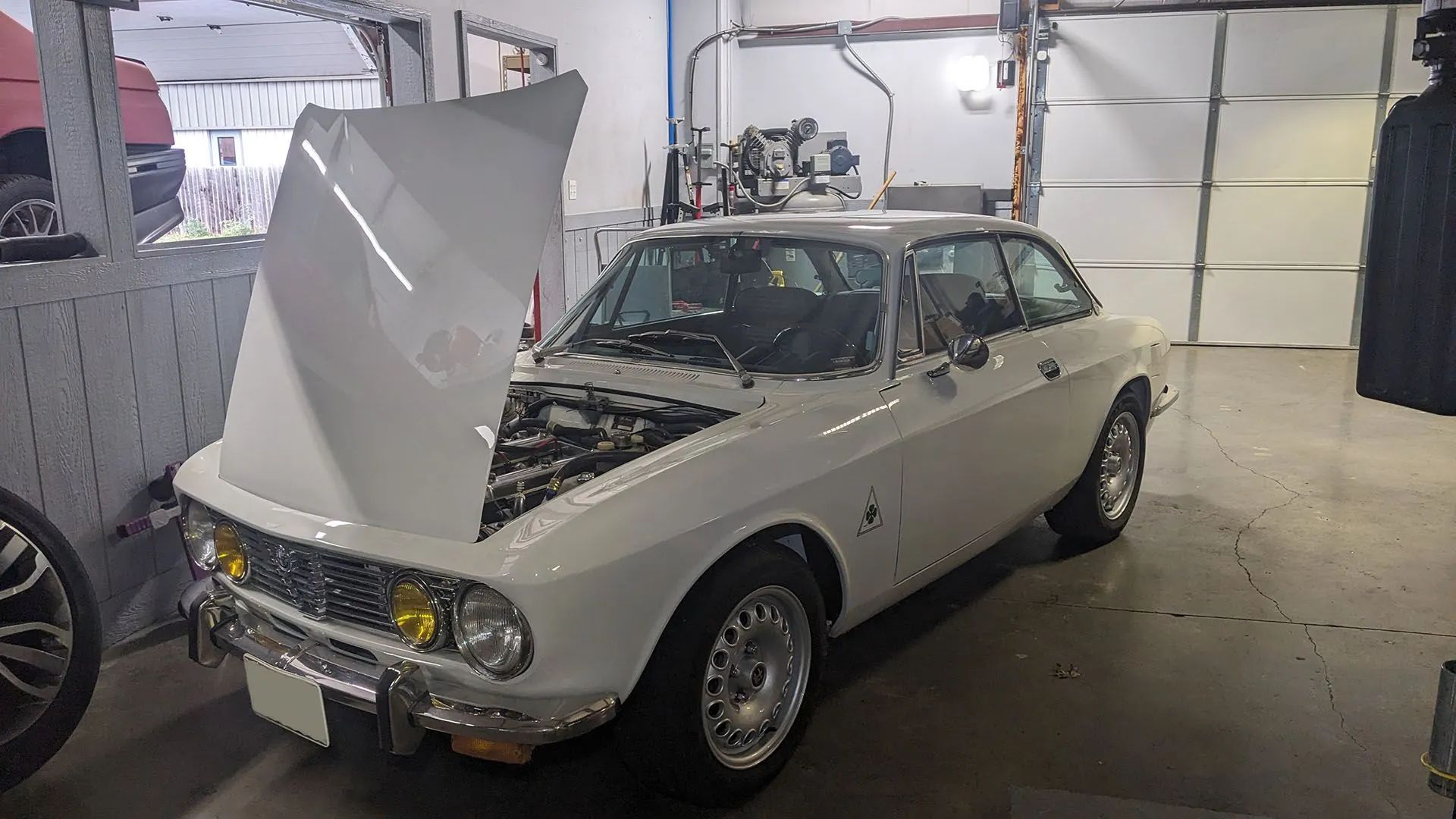 White vintage sports car with hood open in a garage.