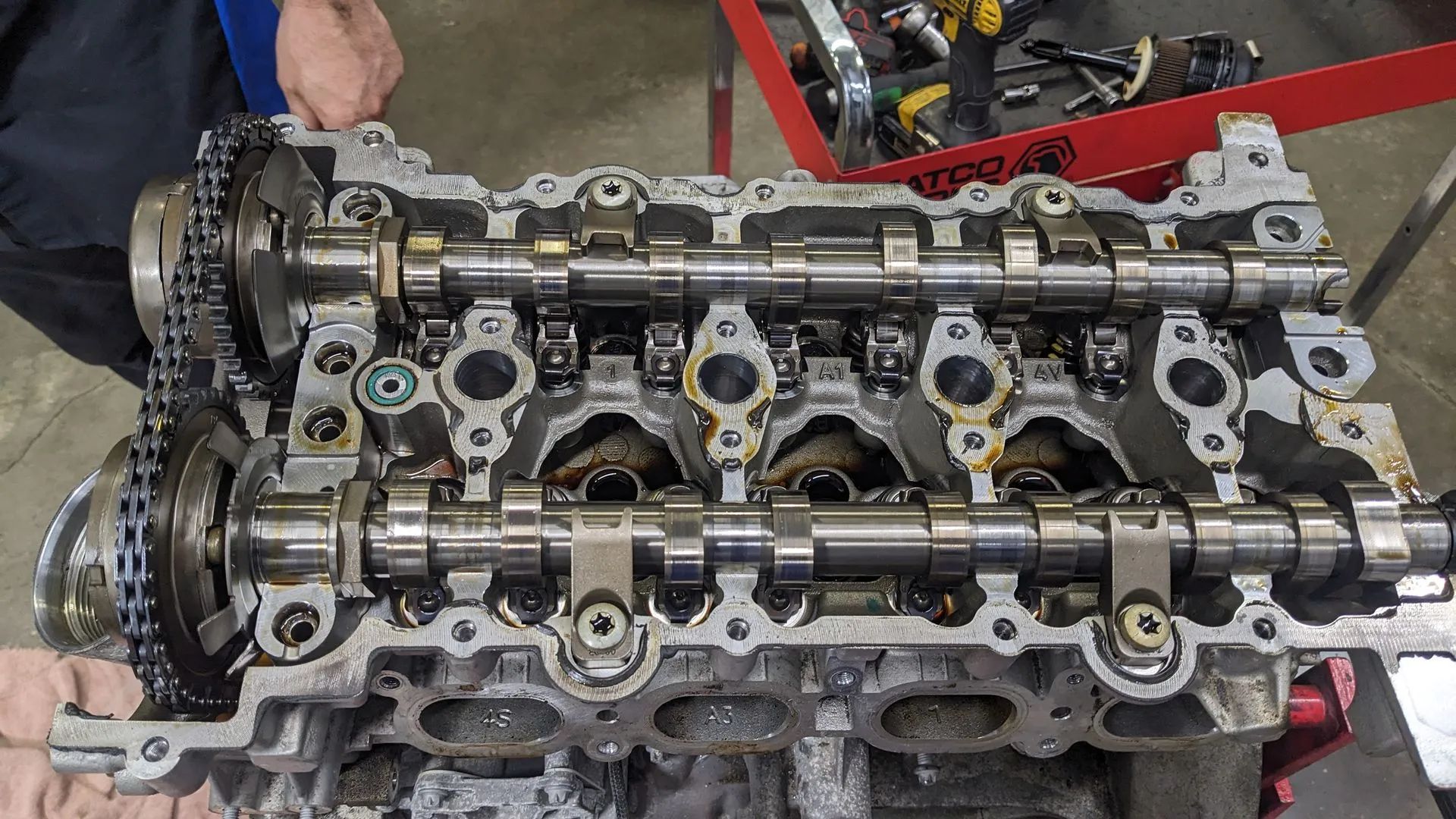 Engine cylinder head with camshafts and timing chain exposed, in a workshop.