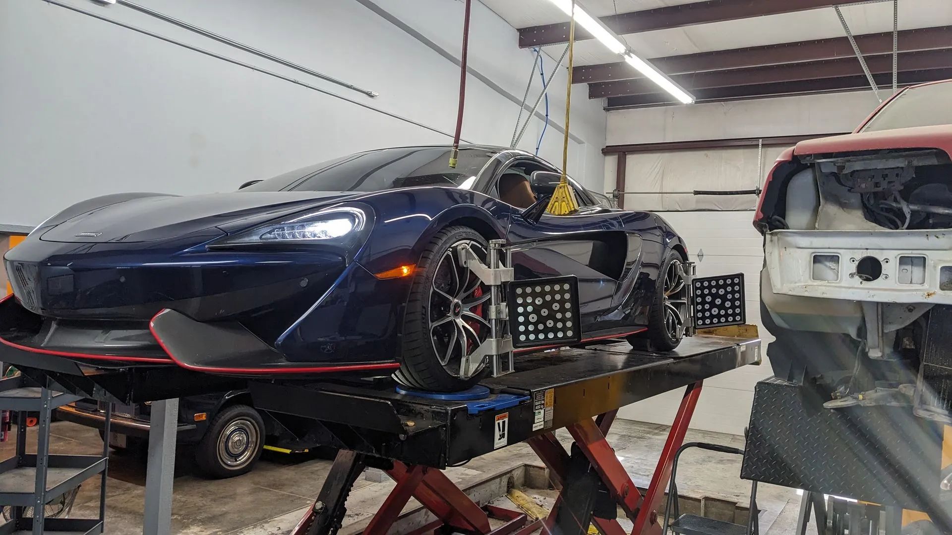 Blue McLaren sports car on a lift in a garage with alignment equipment attached to wheels.