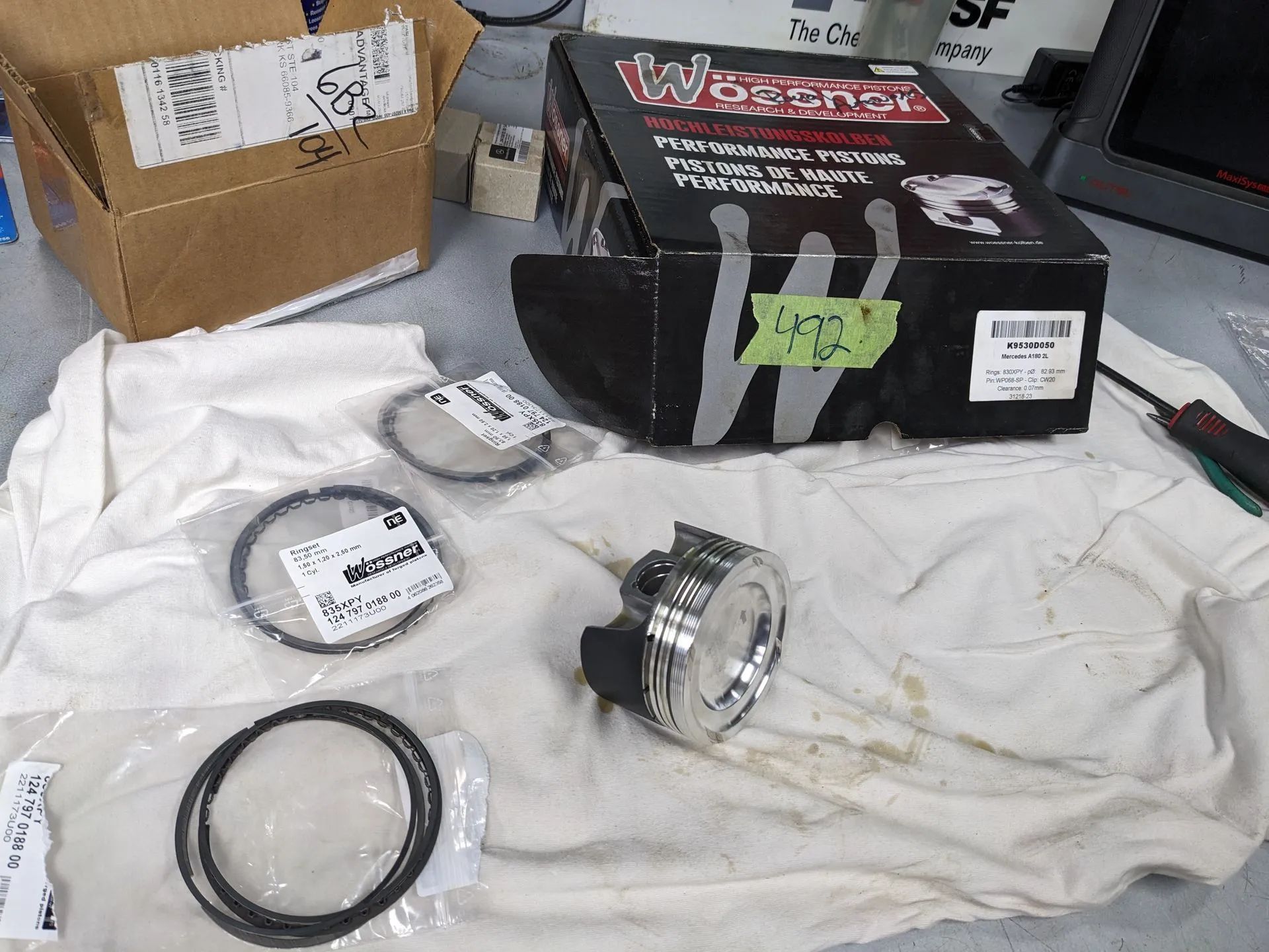 Parts on a white cloth: piston rings, headlight assembly, box labeled 