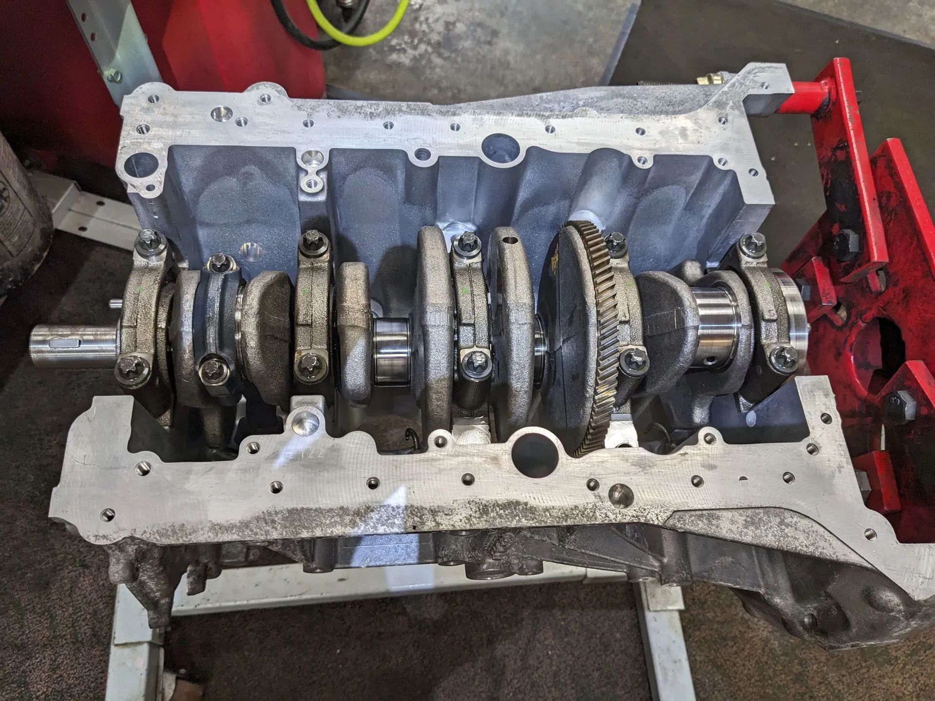 Engine block with crankshaft and connecting rods visible, on a stand in a workshop.