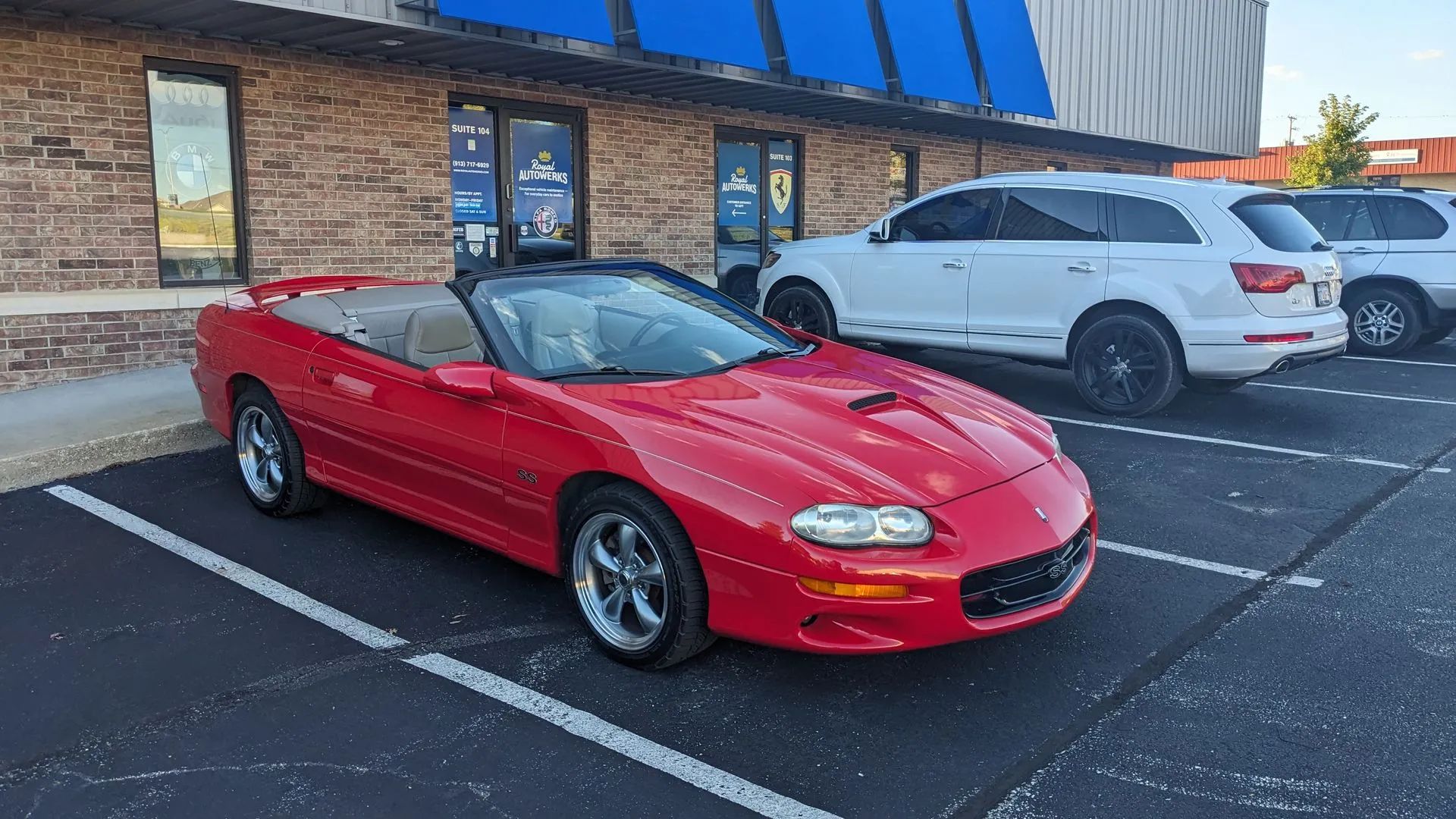 Red convertible sports car parked in front of a brick building. Two SUVs are parked behind it.