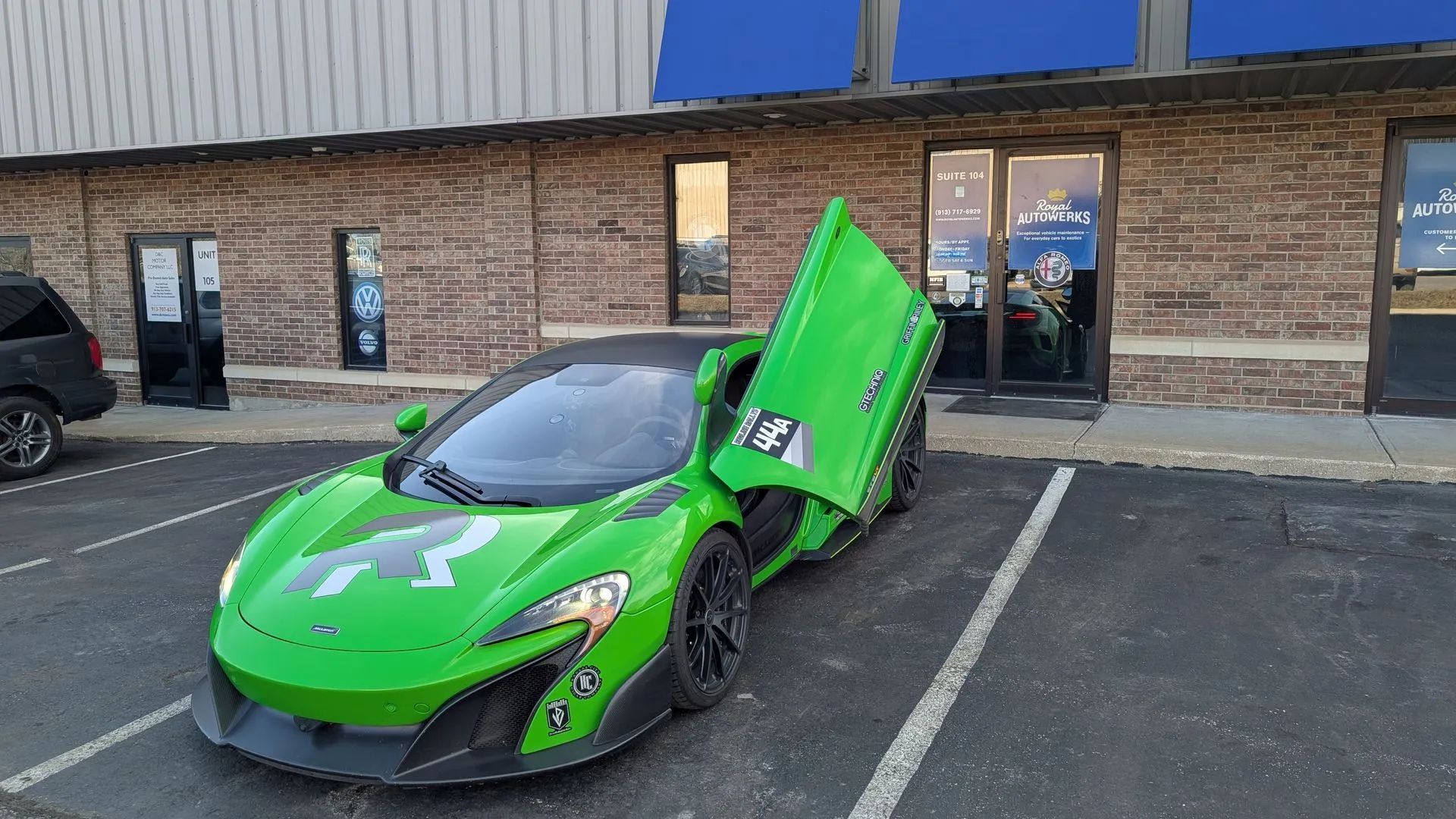 Green sports car with gullwing doors open, parked in front of a brick building.