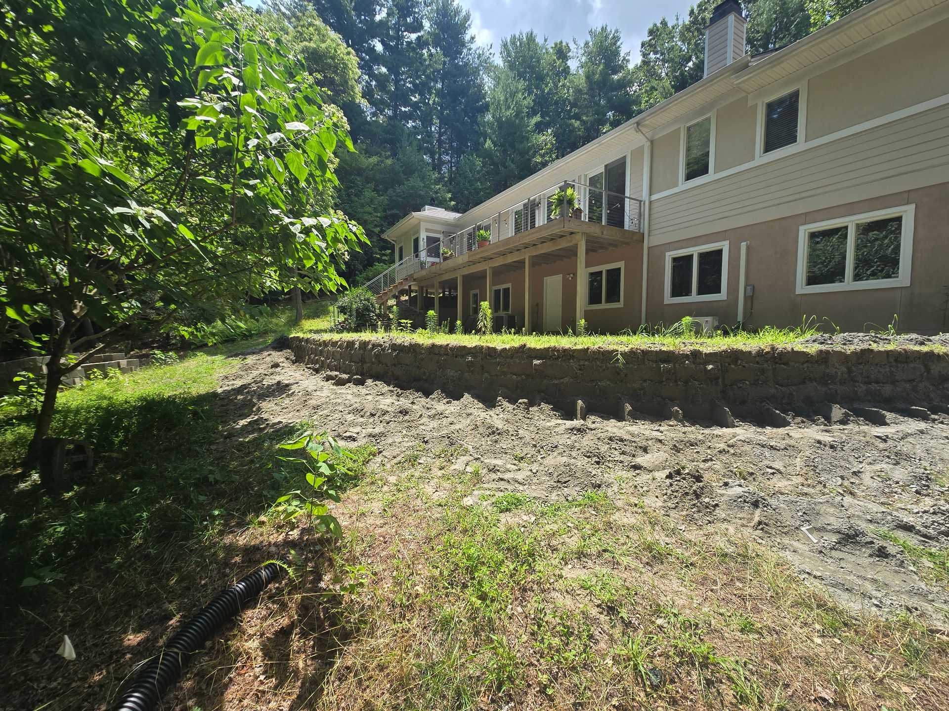 Side view of a beige house with a deck on a hillside with dirt and grass.