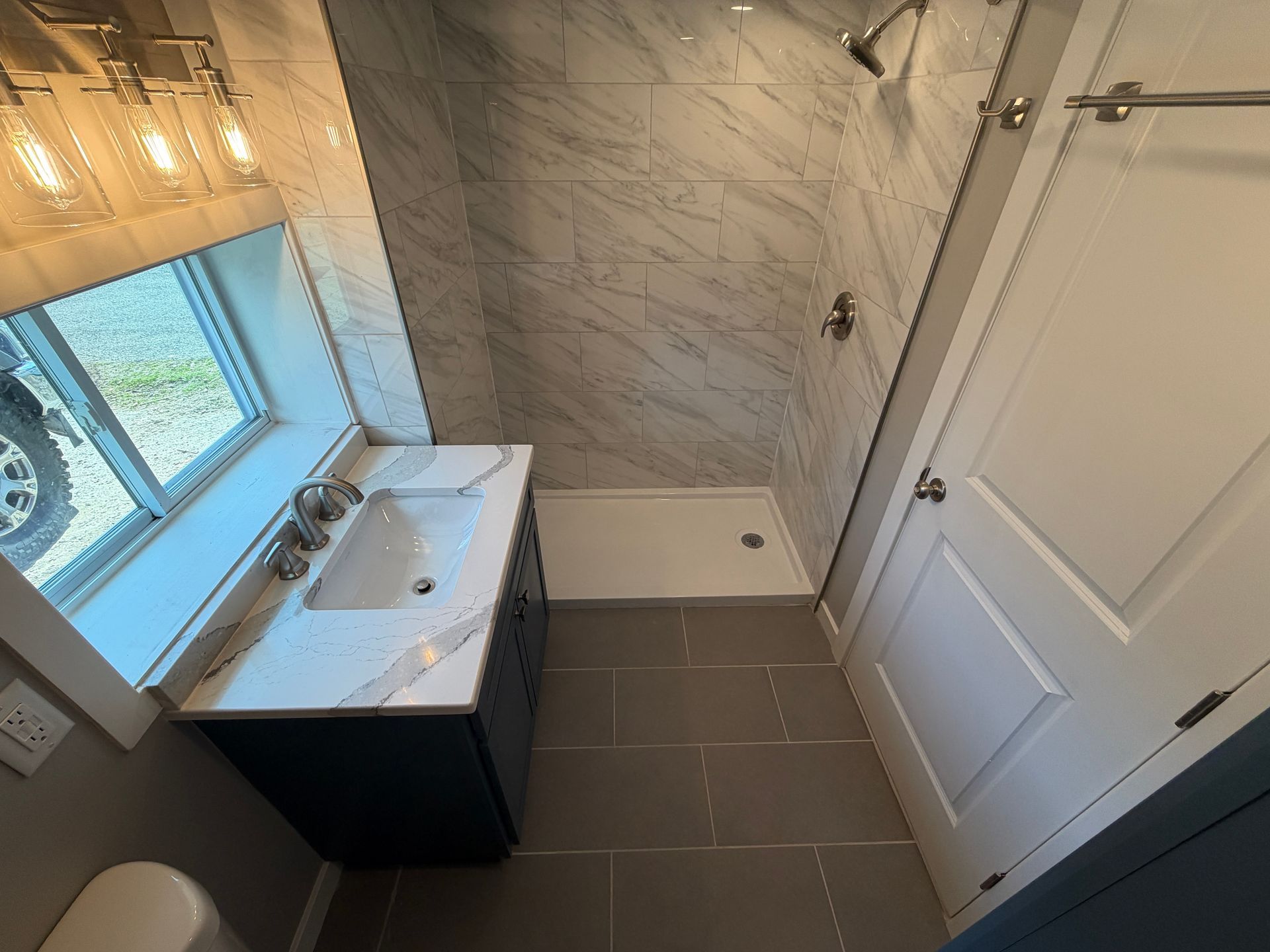 Small bathroom with vanity sink, tiled floor and shower, viewed from the doorway.