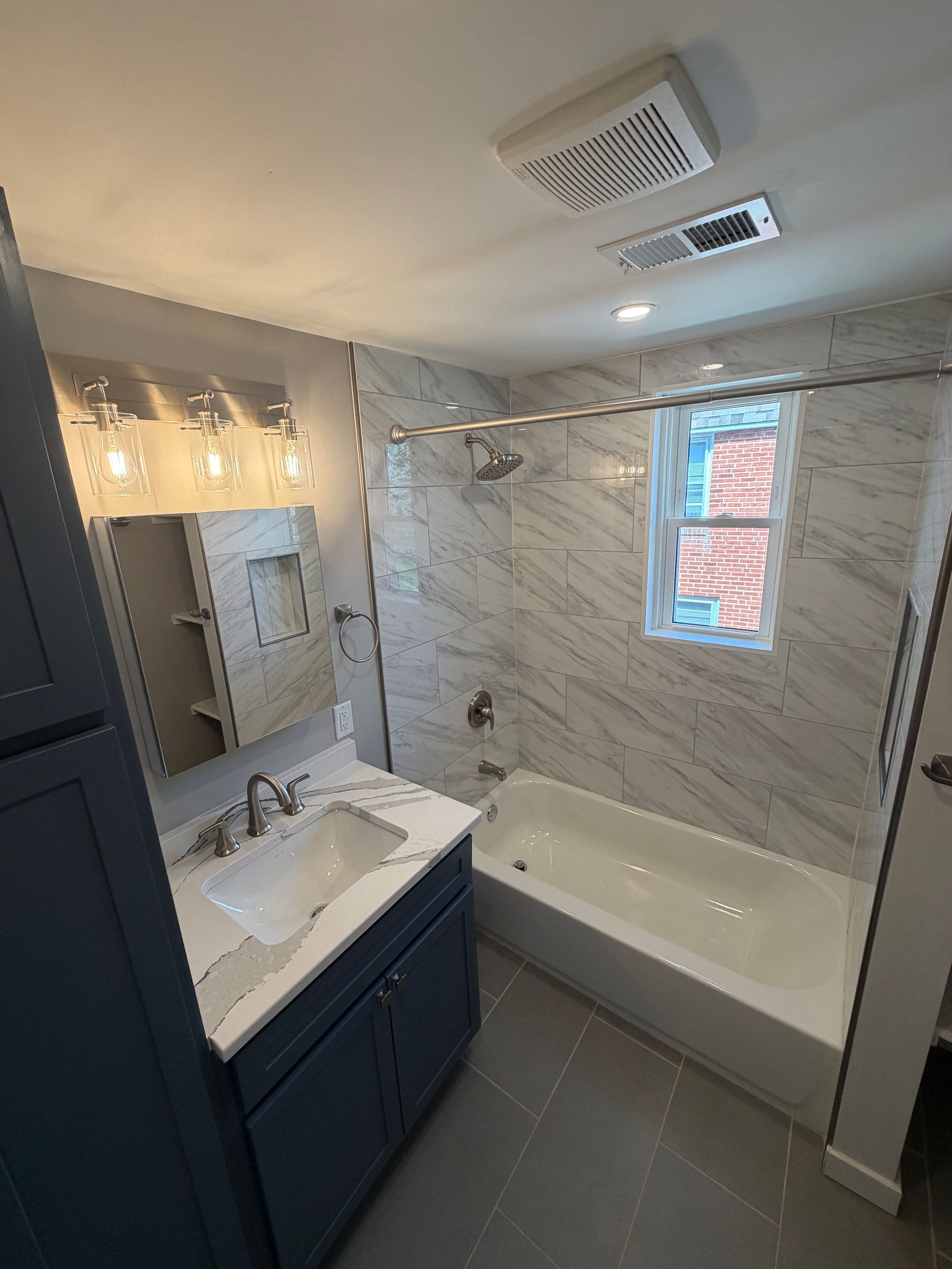 Modern bathroom with double vanity, bathtub, marble-look tile, and gray floor and cabinets.