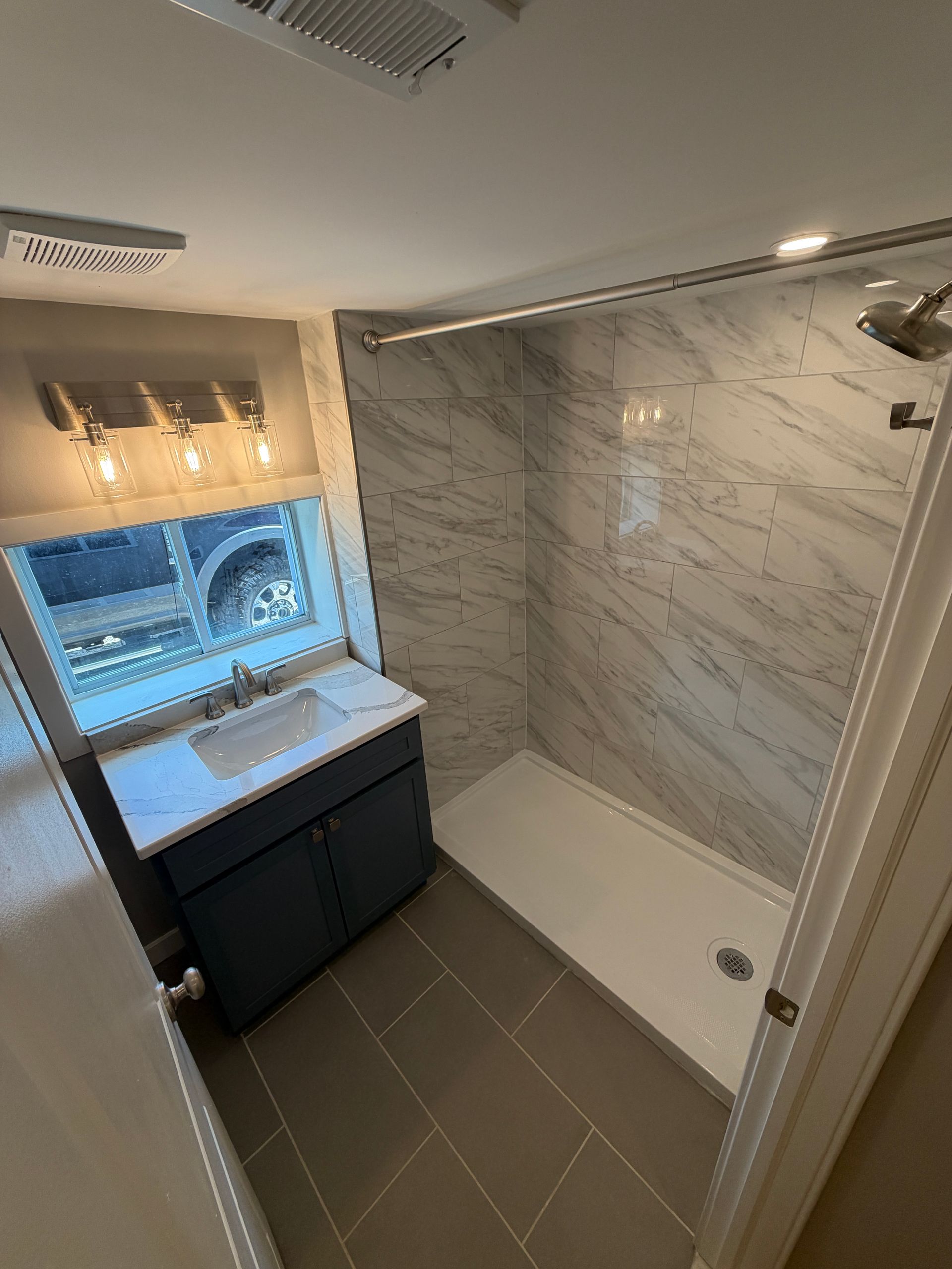 Small modern bathroom with marble-tile shower, vanity, sink, and window