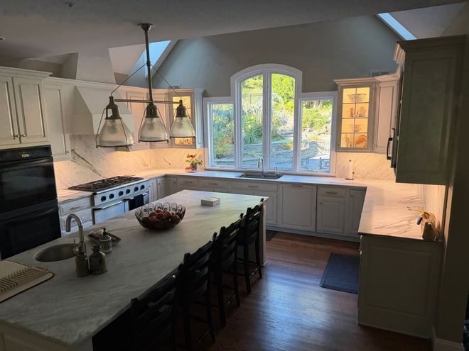 Modern kitchen with white cabinets, marble countertops, large island, and arched window.