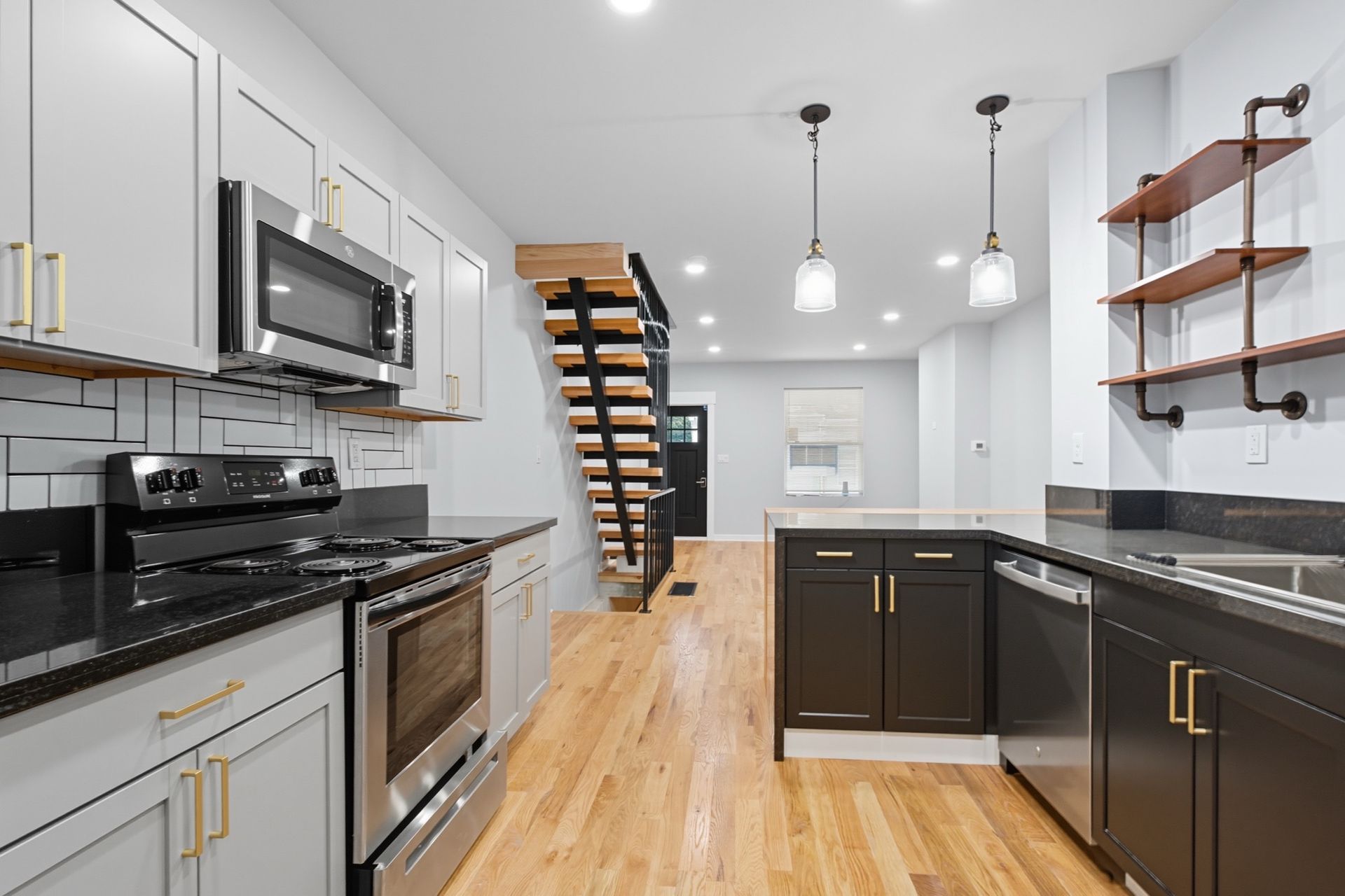 Modern kitchen with gray and dark cabinets, stainless steel appliances, and wooden floor.