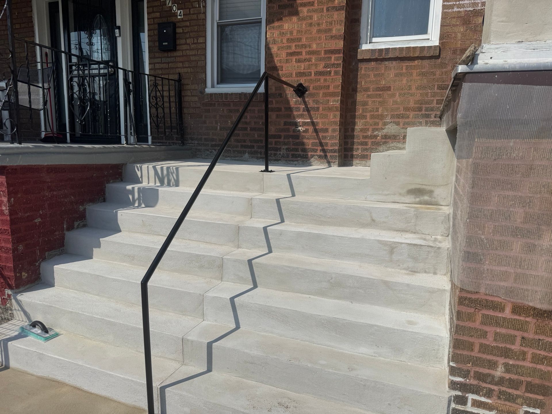 Exterior concrete steps with a black handrail leading to a brick building's entrance.