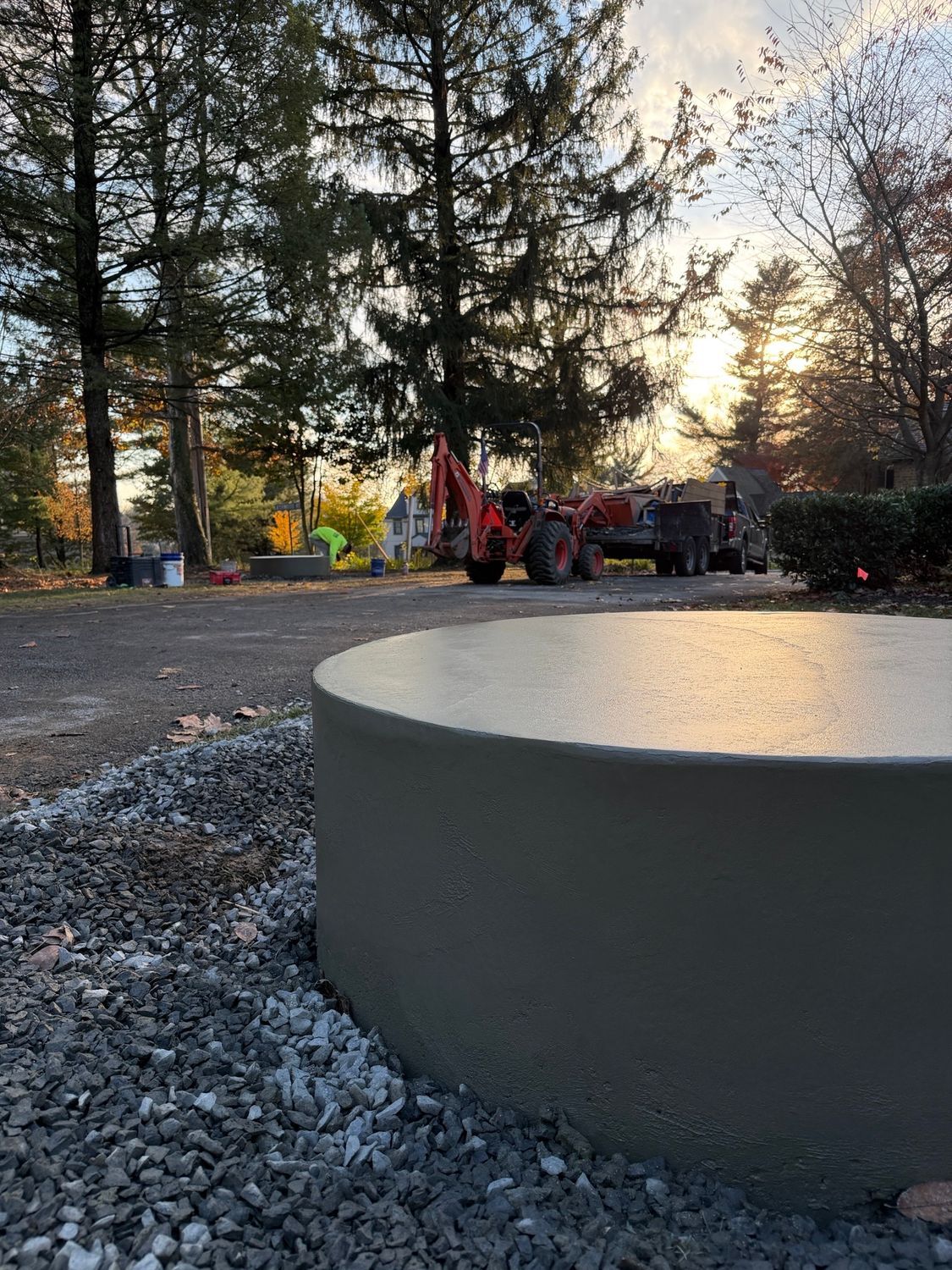 A newly constructed concrete circular structure with construction vehicles in the background. Gravel and trees present.